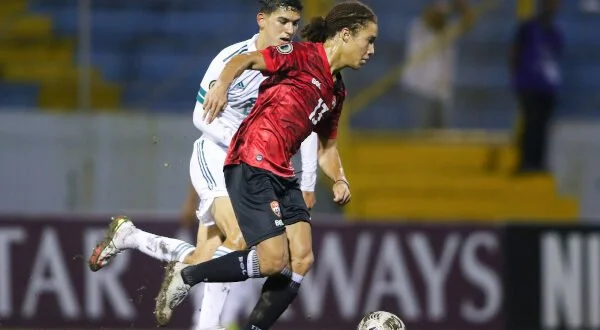Two soccer players competing for the ball during a match, with one wearing a white uniform and the other a red uniform.
