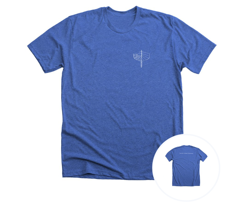 A blue T-shirt with a small white line drawing of a sailboat on the front left chest area, and the back has text that reads 'The Art of Boat Buliding'