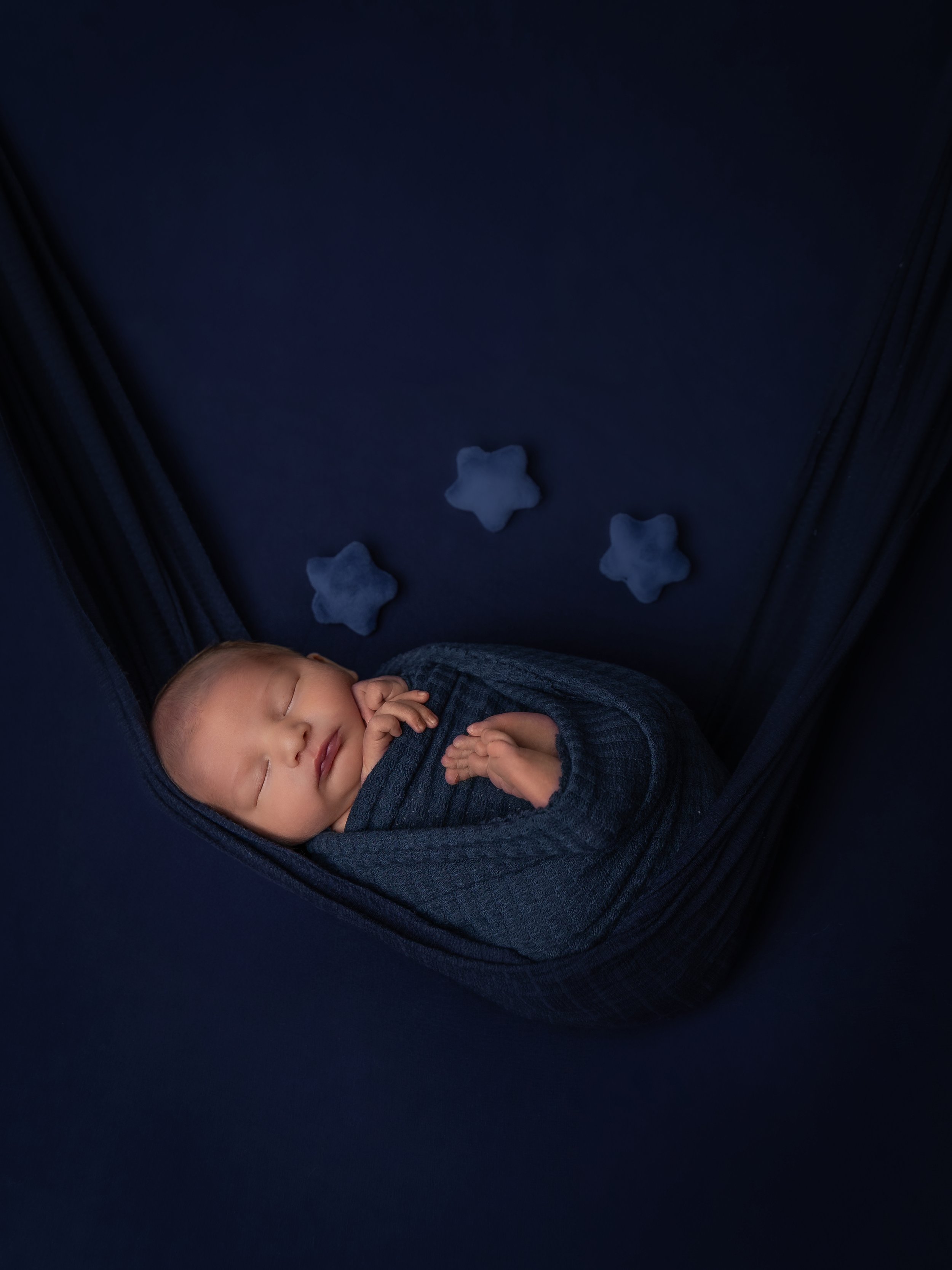 The image depicts a newborn baby peacefully sleeping, snugly wrapped in a blue swaddle. The color scheme is soothing blue hues with stars.
