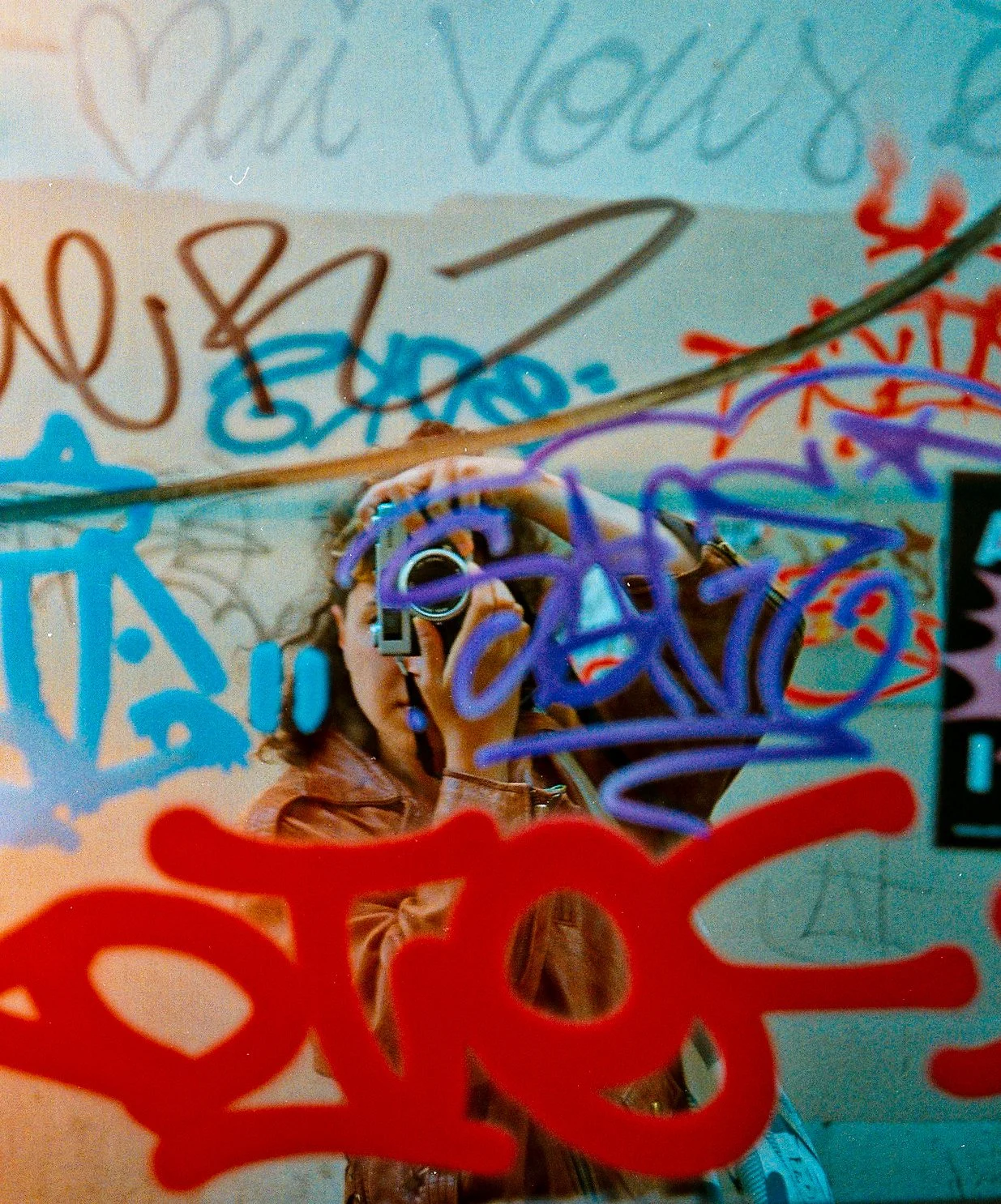 Reflet d'une personne prenant une photo avec un appareil photo dans un miroir couvert de graffiti coloré