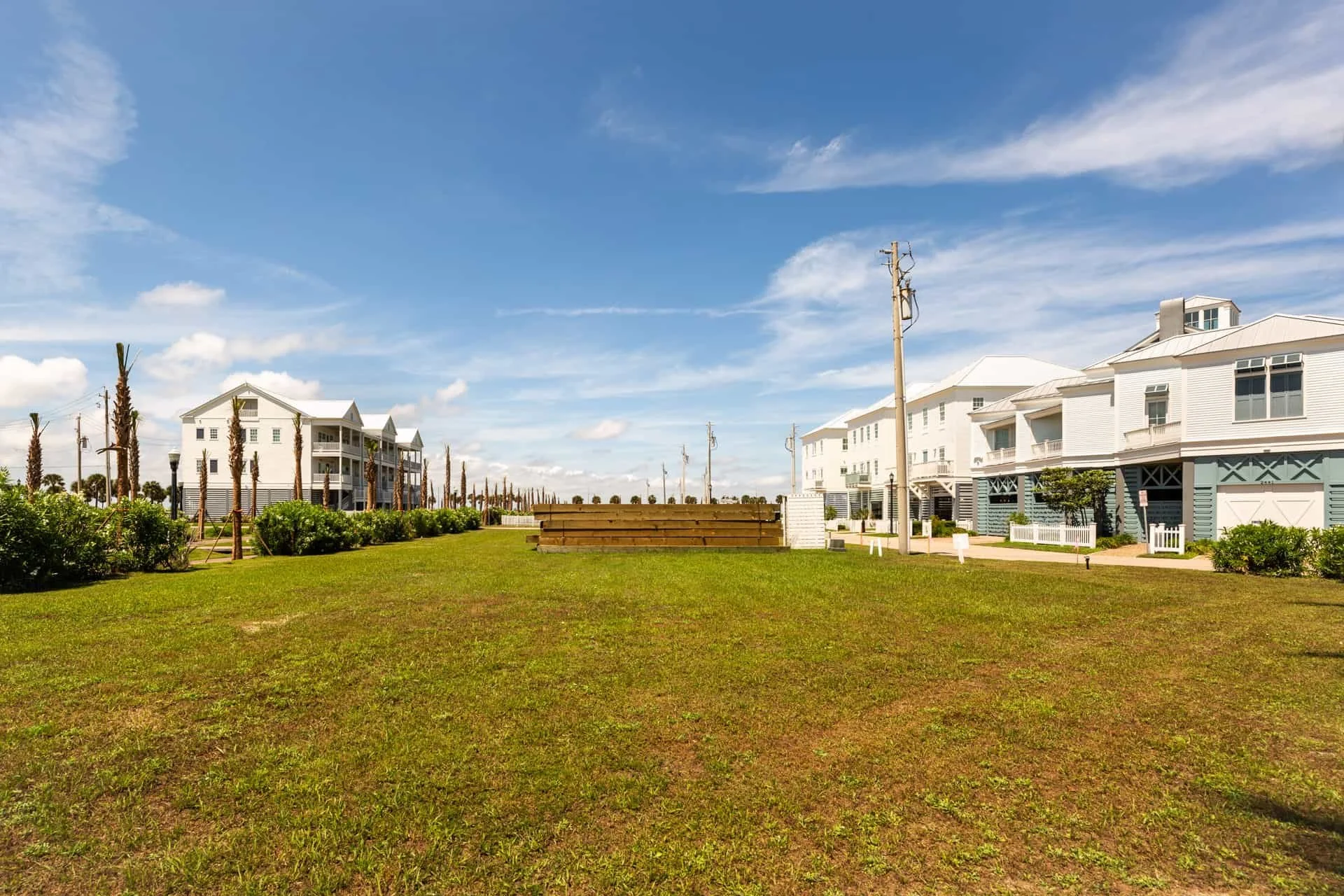 A sunny day view of a row of beach houses with a well-maintained grassy area in the foreground and a blue sky with some clouds above.