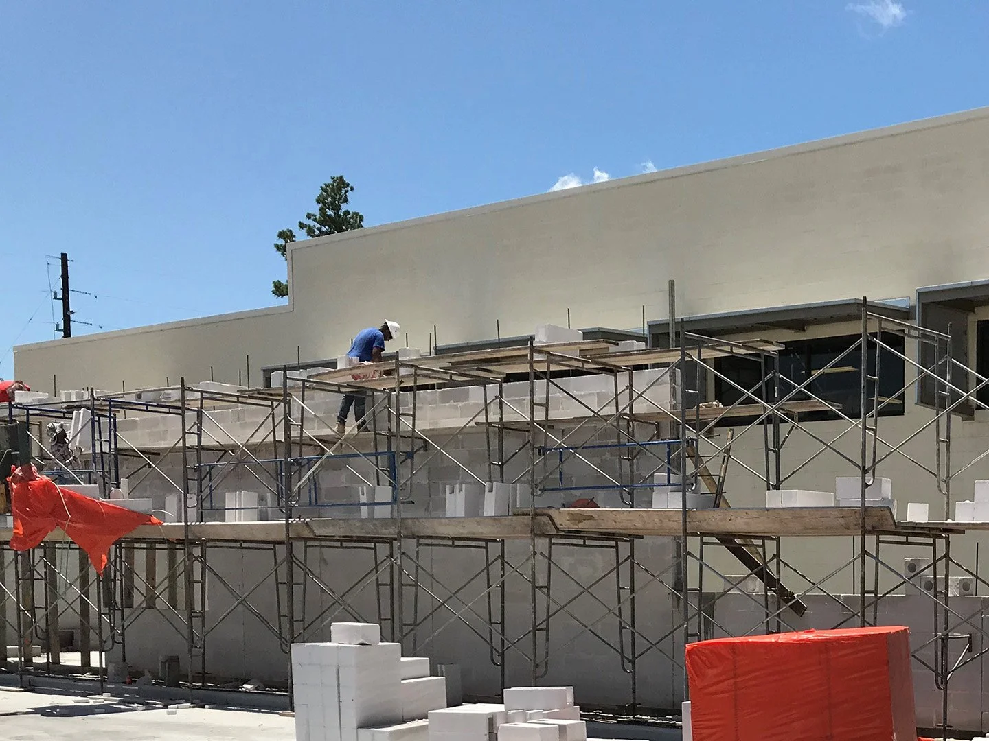 Construction workers building a modern, white commercial or residential building with scaffolding and foam insulation panels, under a clear blue sky.