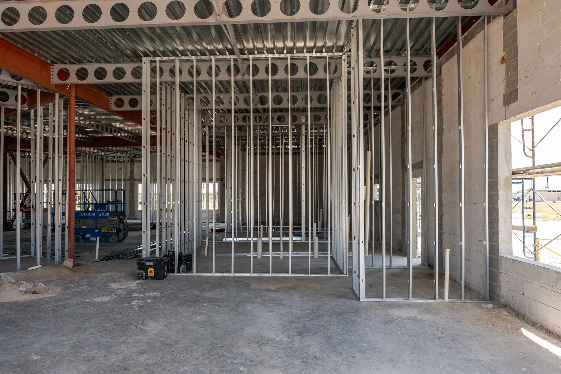 Interior of a building under construction with metal framing for walls and ceiling, and some construction equipment on the floor.