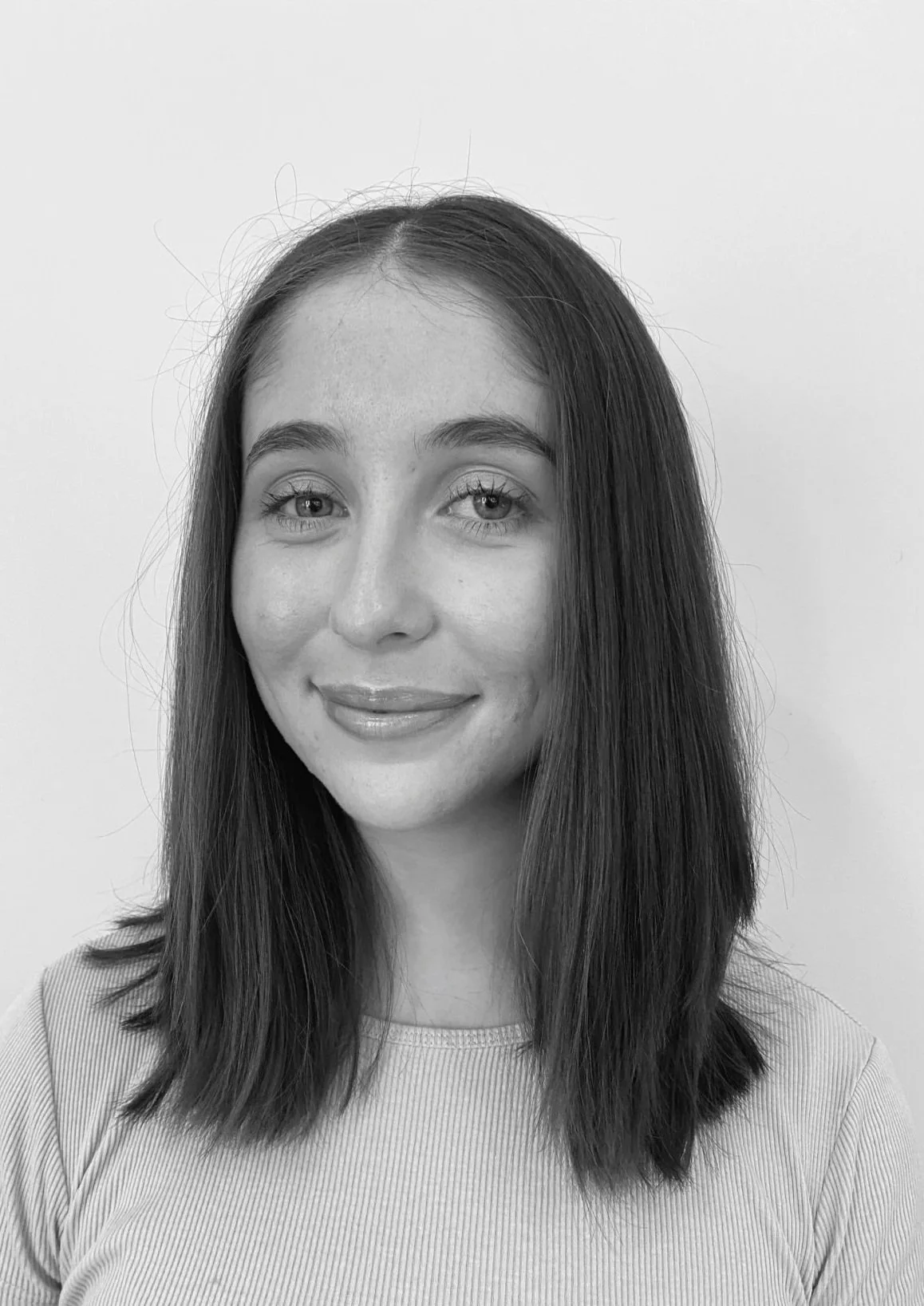 Black and white portrait of a young woman with shoulder-length hair, smiling, wearing a striped top, standing against a plain background.