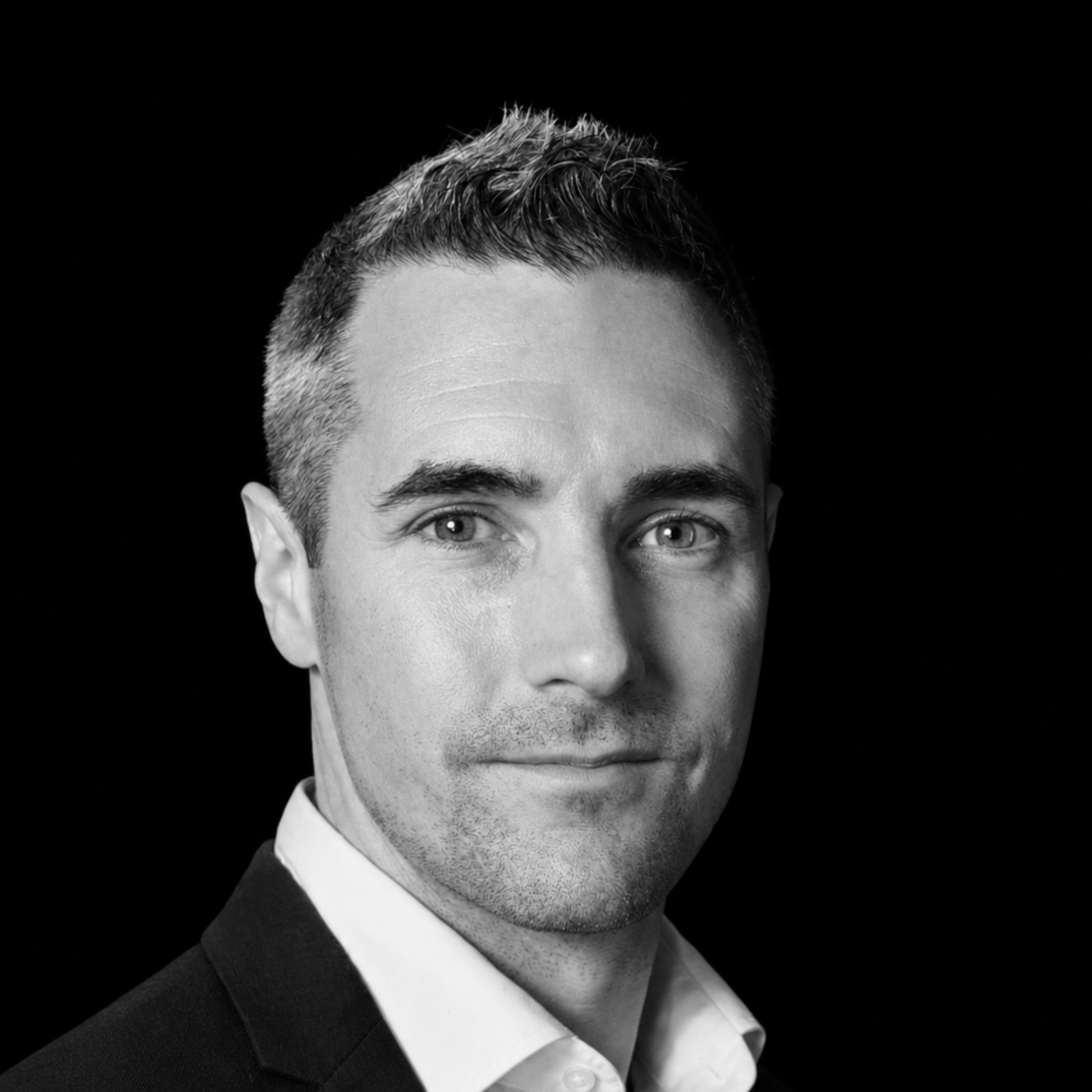 Black and white portrait of a man with short hair, wearing a collared shirt, looking directly at the camera.