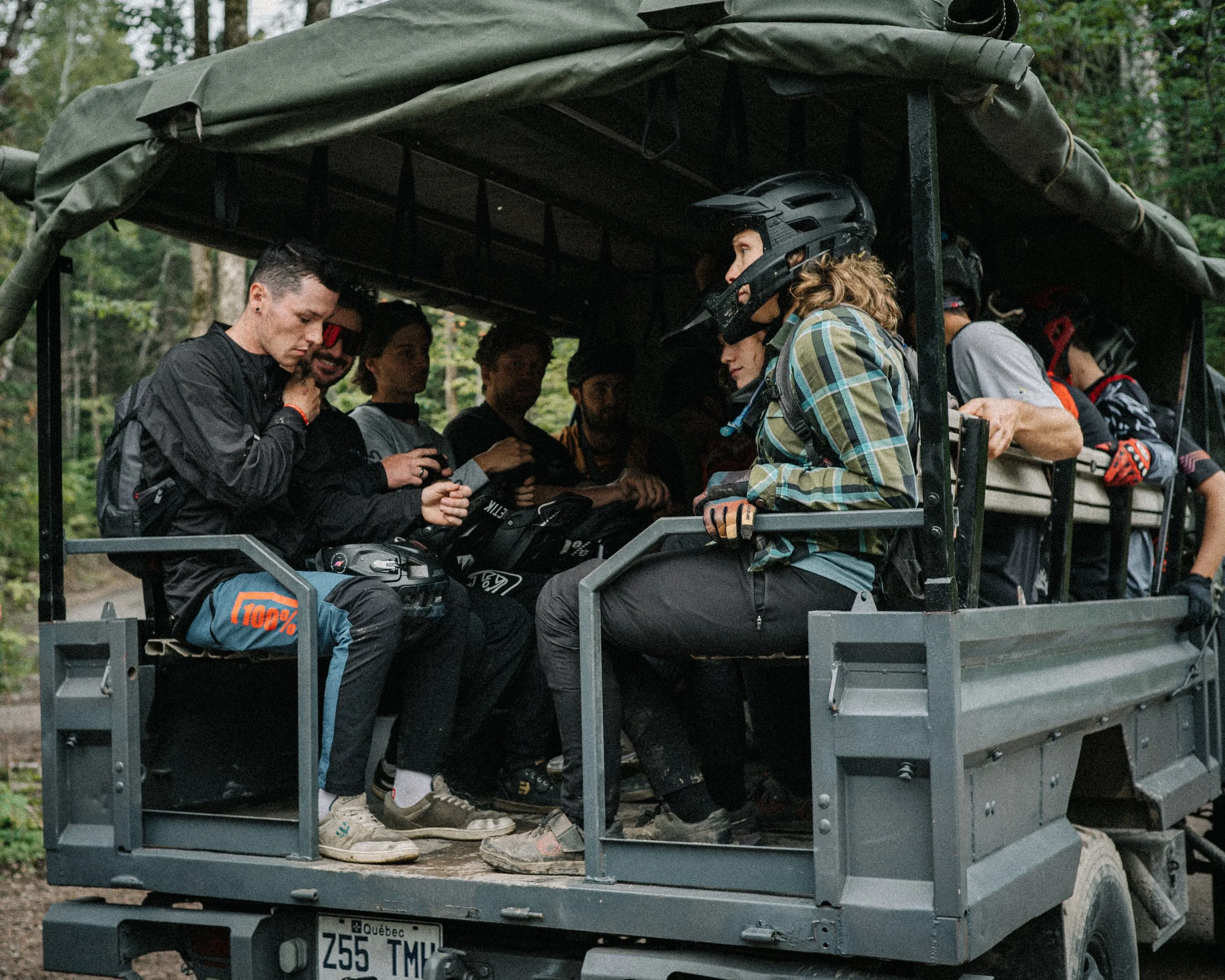 Groupe de personnes dans un véhicule tout-terrain, portant des équipements de protection et des casques, entouré de forêt.