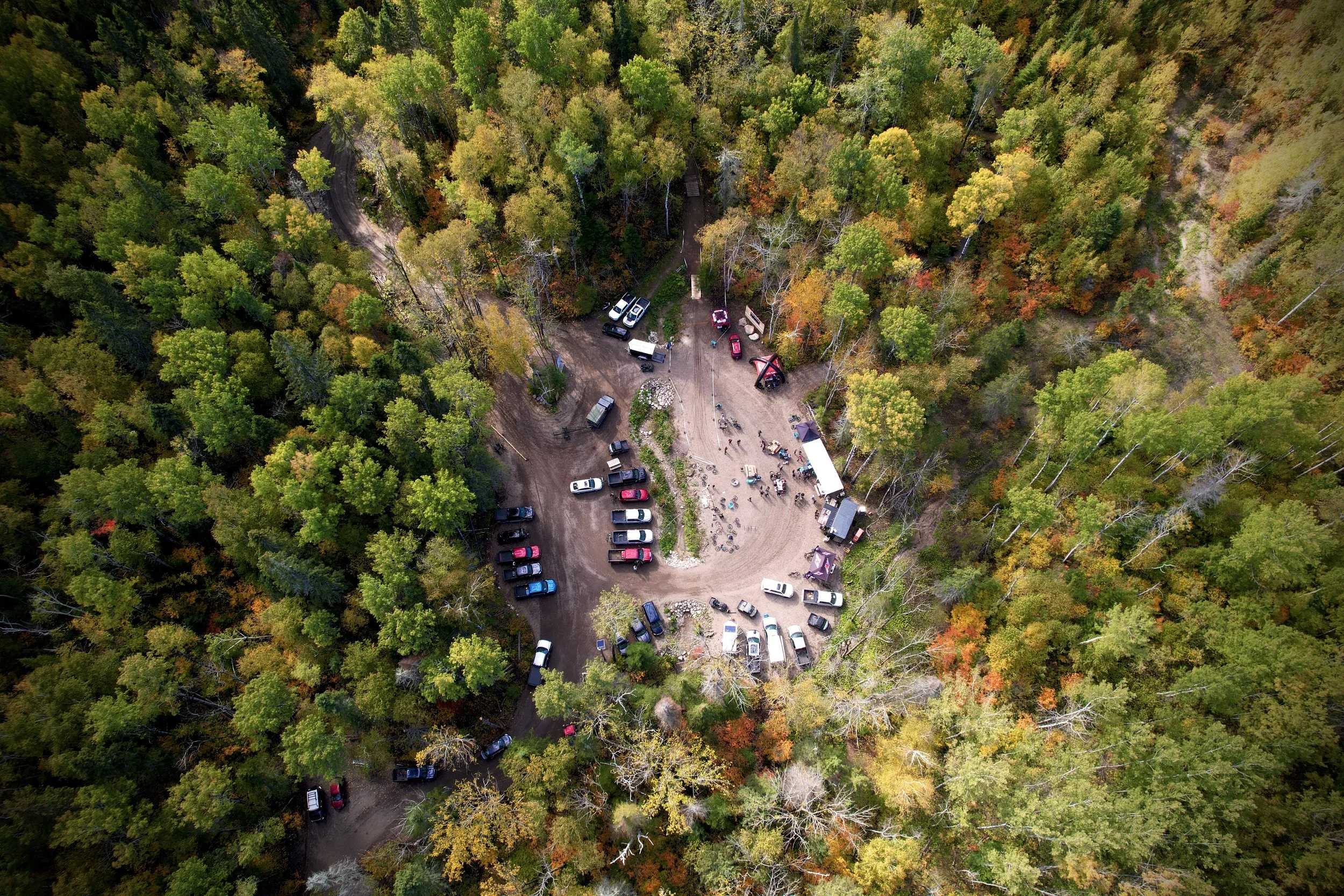 Vue aérienne d'une clairière dans une forêt avec des véhicules et des personnes rassemblés pour un événement ou une activité de plein air.