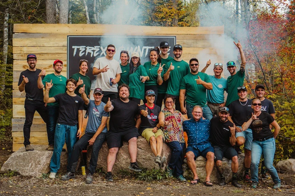 Groupe de personnes posant ensemble à l'extérieur, devant un panneau 'Terex Quanter', souriant et levant les pouces."