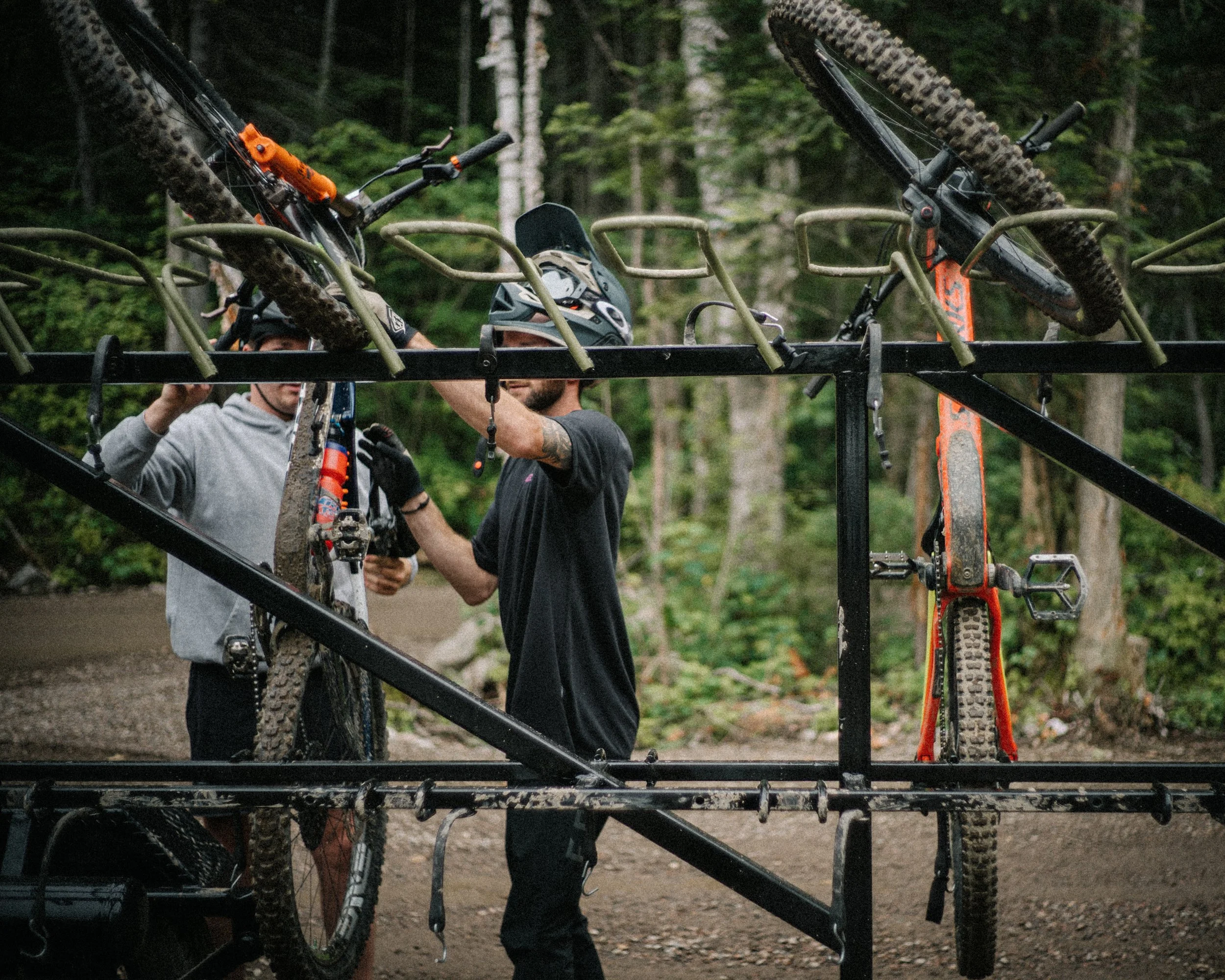 Deux personnes chargent des vélos tout-terrain sur un support de transport en métal dans une zone boisée.