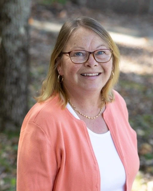 A woman with glasses and blonde hair smiling outdoors