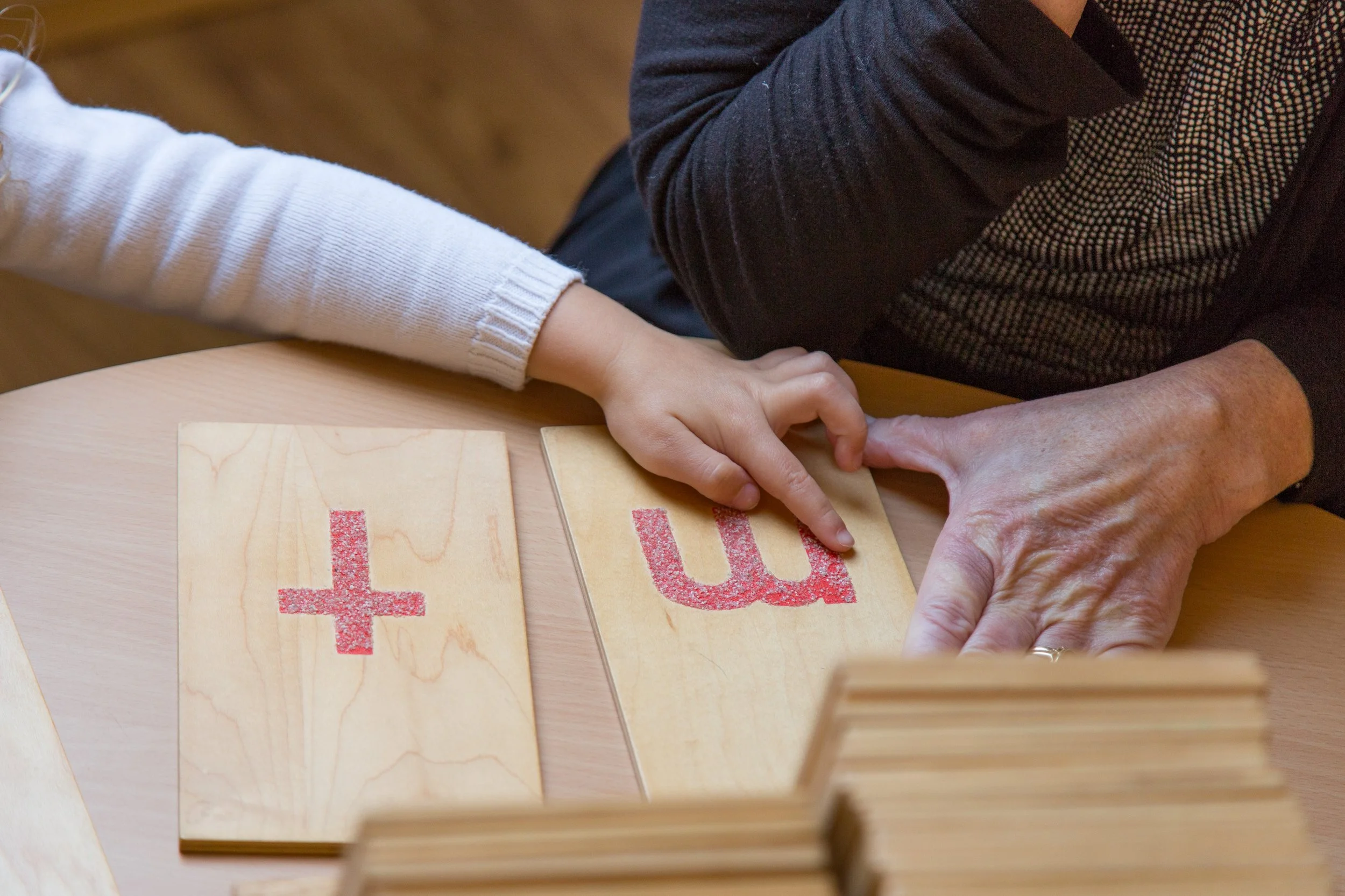 A child receiving a lesson with sandpaper letters at a table.