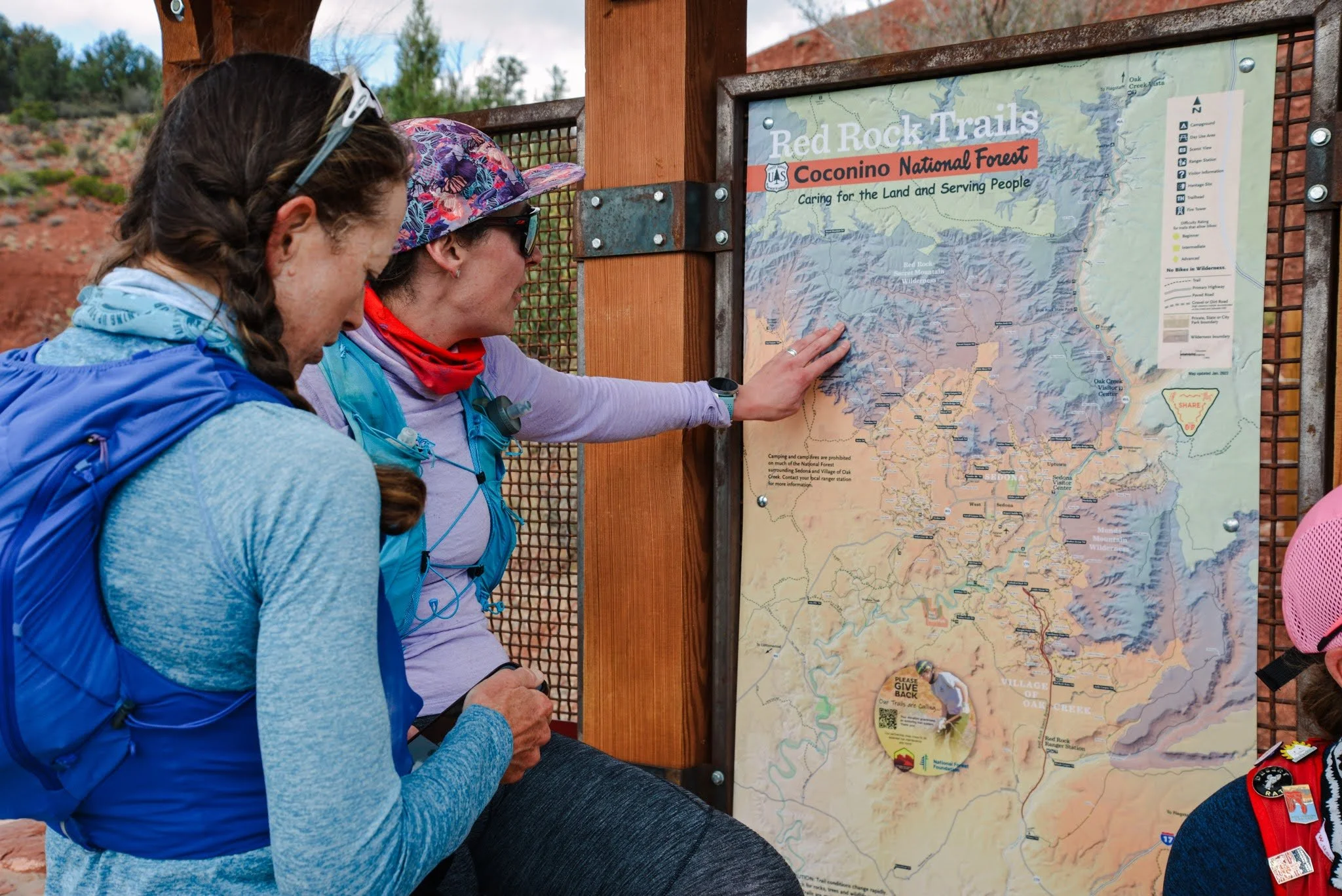 Three women outdoors looking at a map of Red Rock Trails in Coconino National Forest.