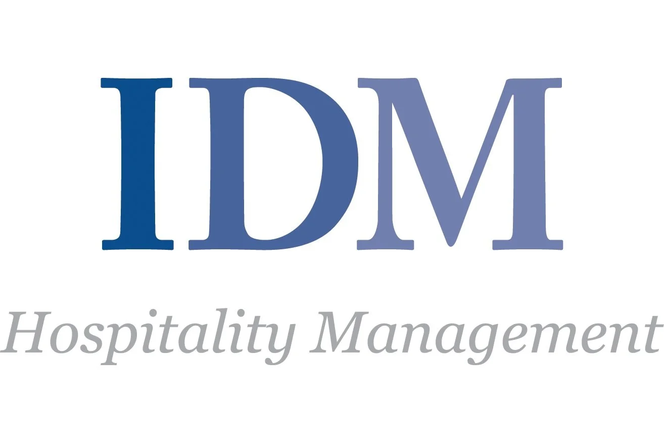 Logo for the company IDM Hospitality Management with large blue letters "IDM" and the words "Hospitality Management" in smaller, gray italics below.
