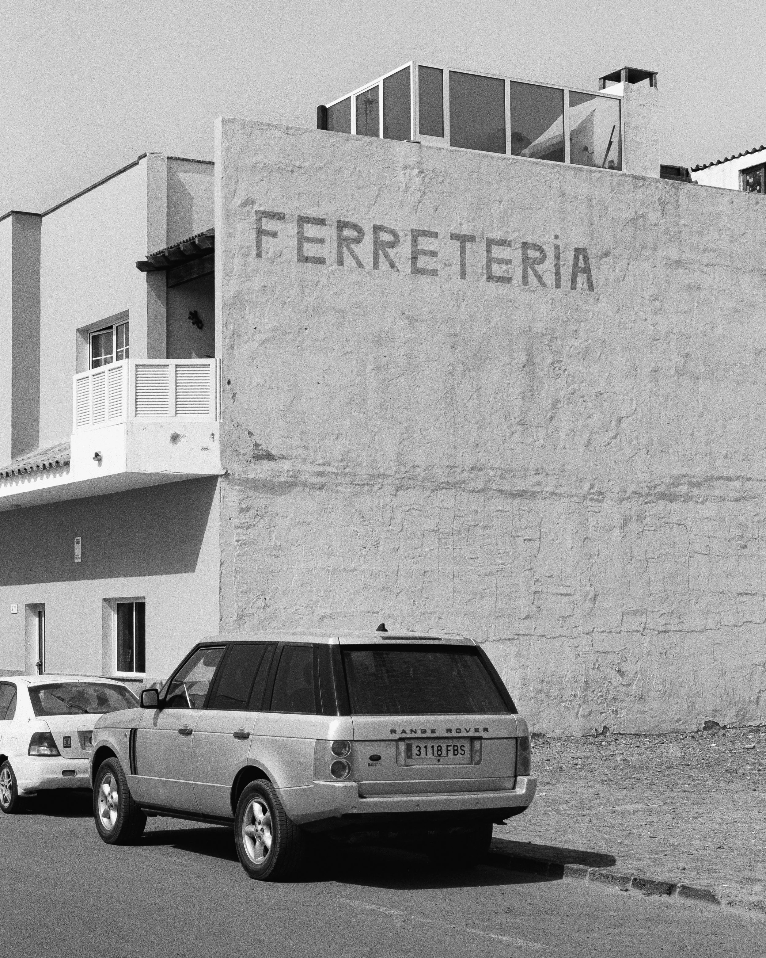 A black and white photo of a building with the word 'FERRETERIA' painted on the wall, along with parked cars in front.