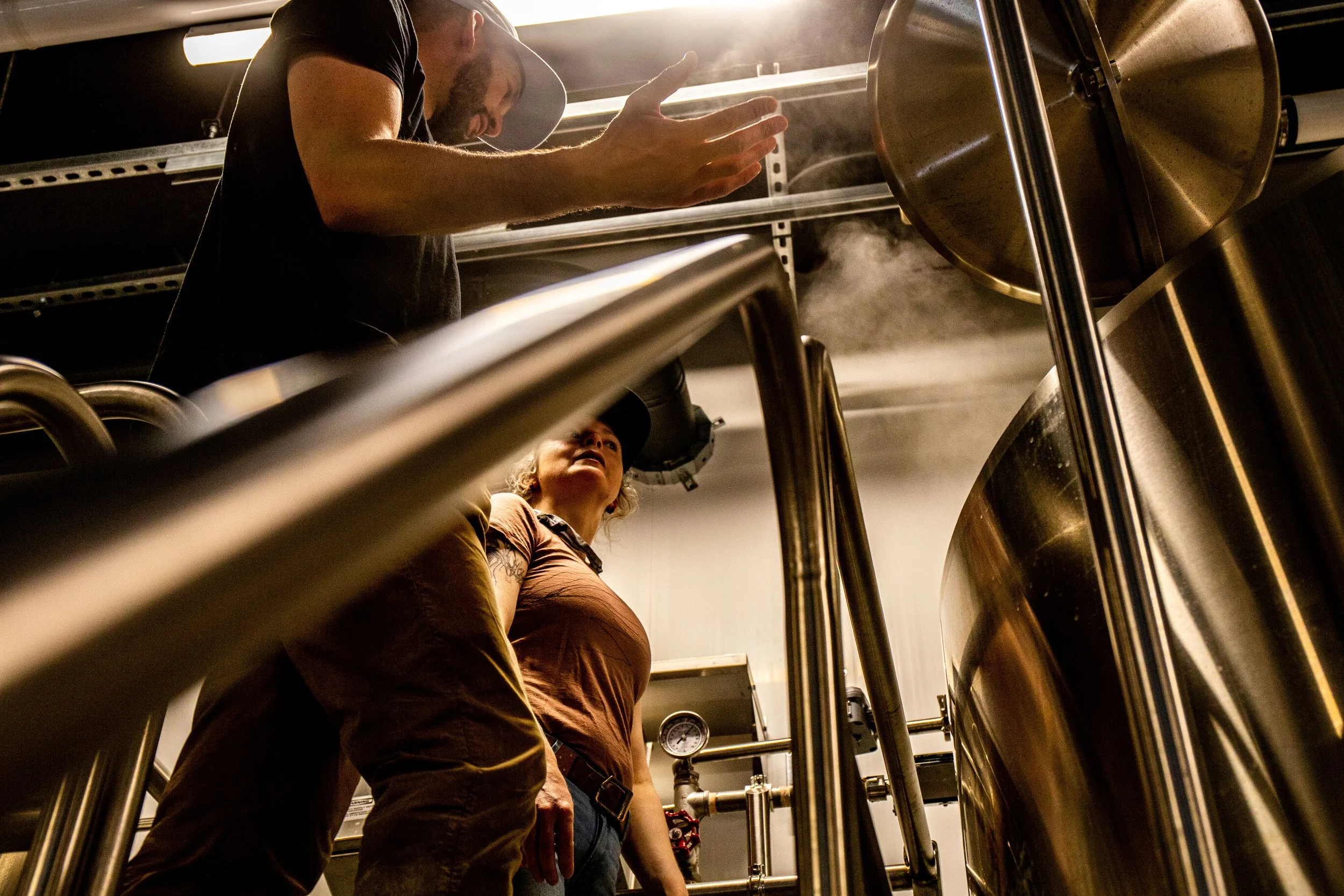 People working in a brewery, with stainless steel tanks and steam.