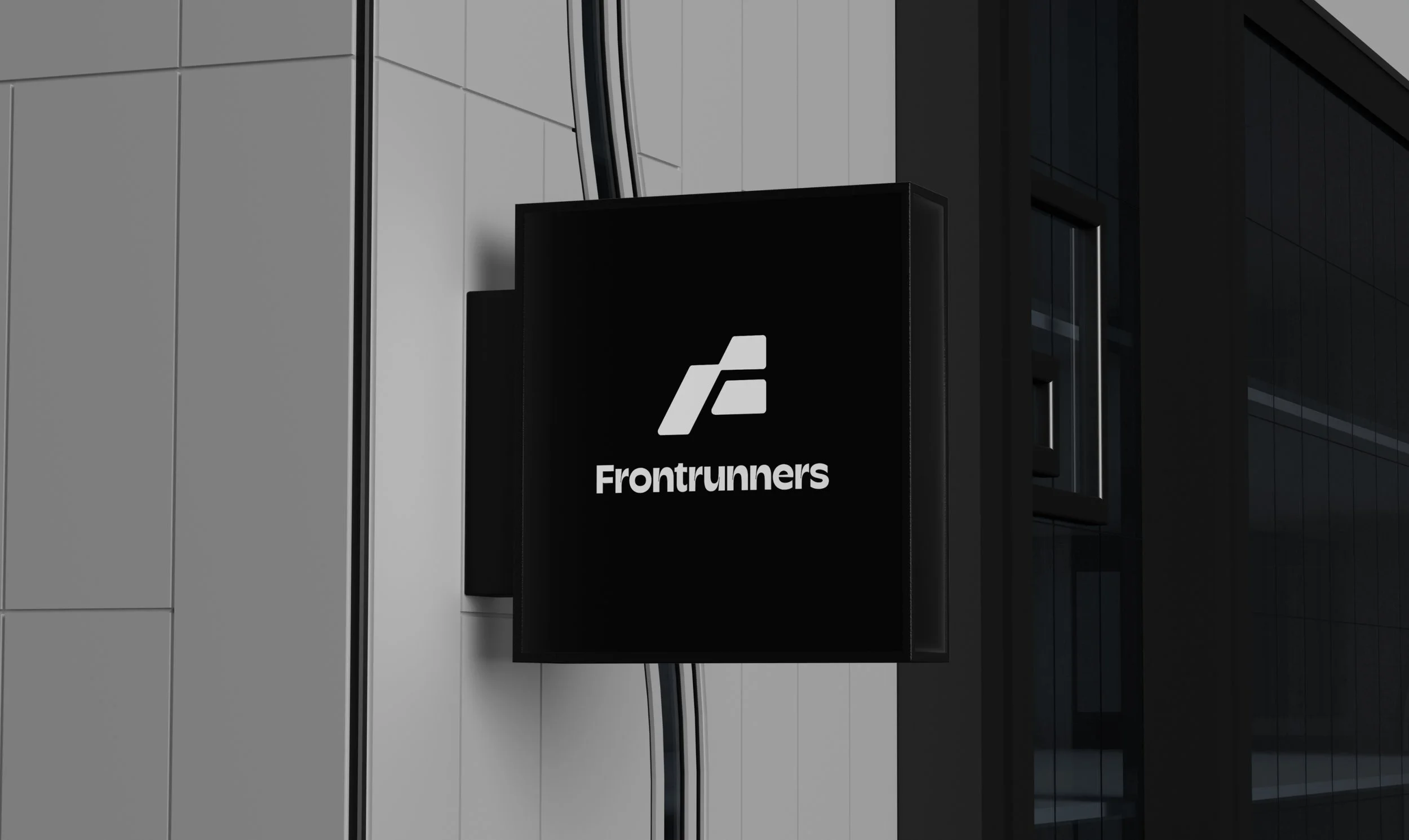 A black sign with the Frontrunners logo and text mounted on an exterior wall of a building.