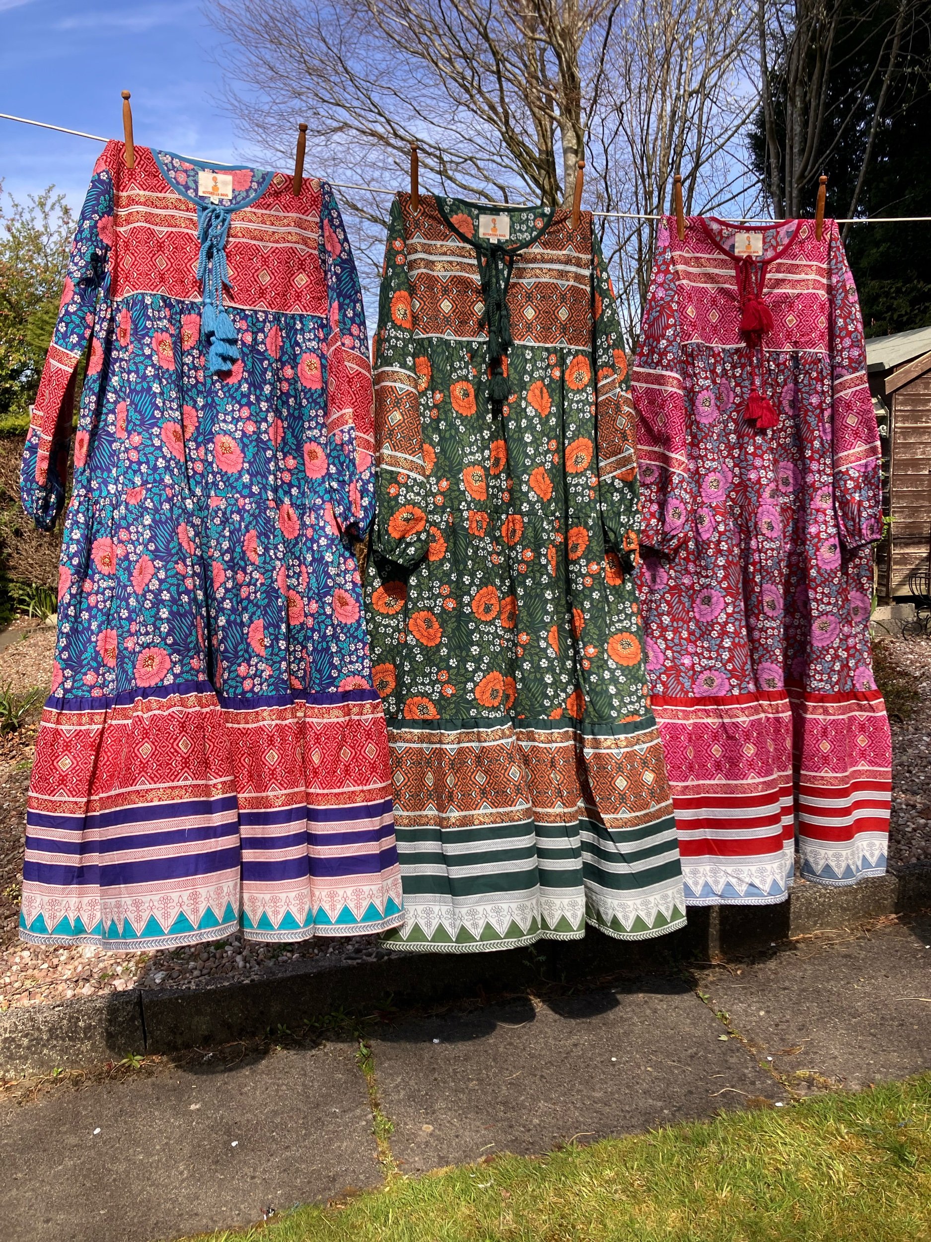 Three colorful floral and geometric patterned dresses hanging on a line outdoors.