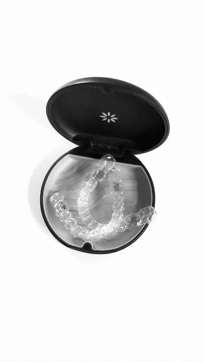 A black case with a floral design inside, holding a transparent dental aligner.