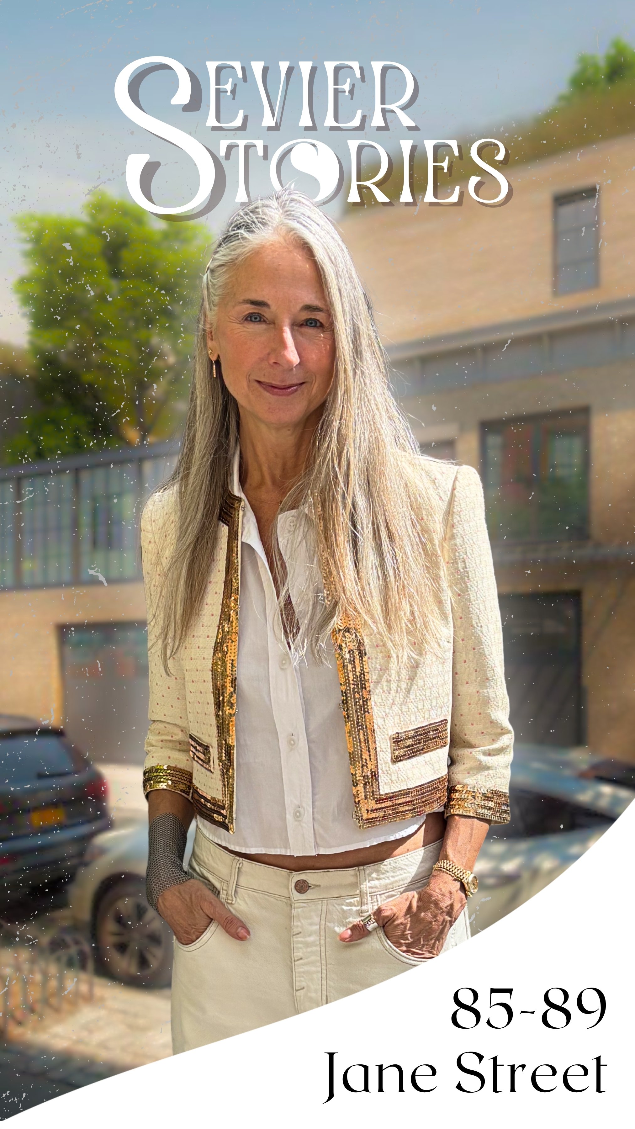 A woman with long, gray hair standing outdoors in front of a building and trees, wearing a cream-colored jacket with decorative accents, a white shirt, and cream pants. The image has text overlay: "Summer Stories," and additional text at the bottom that reads "85-89 Jane Street."