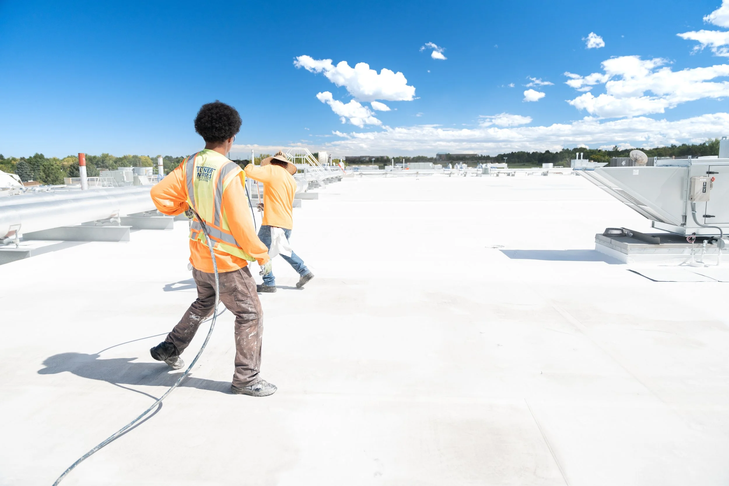 Two Denver commercial roofers wearing safety vests and hard hats on a large flat rooftop.