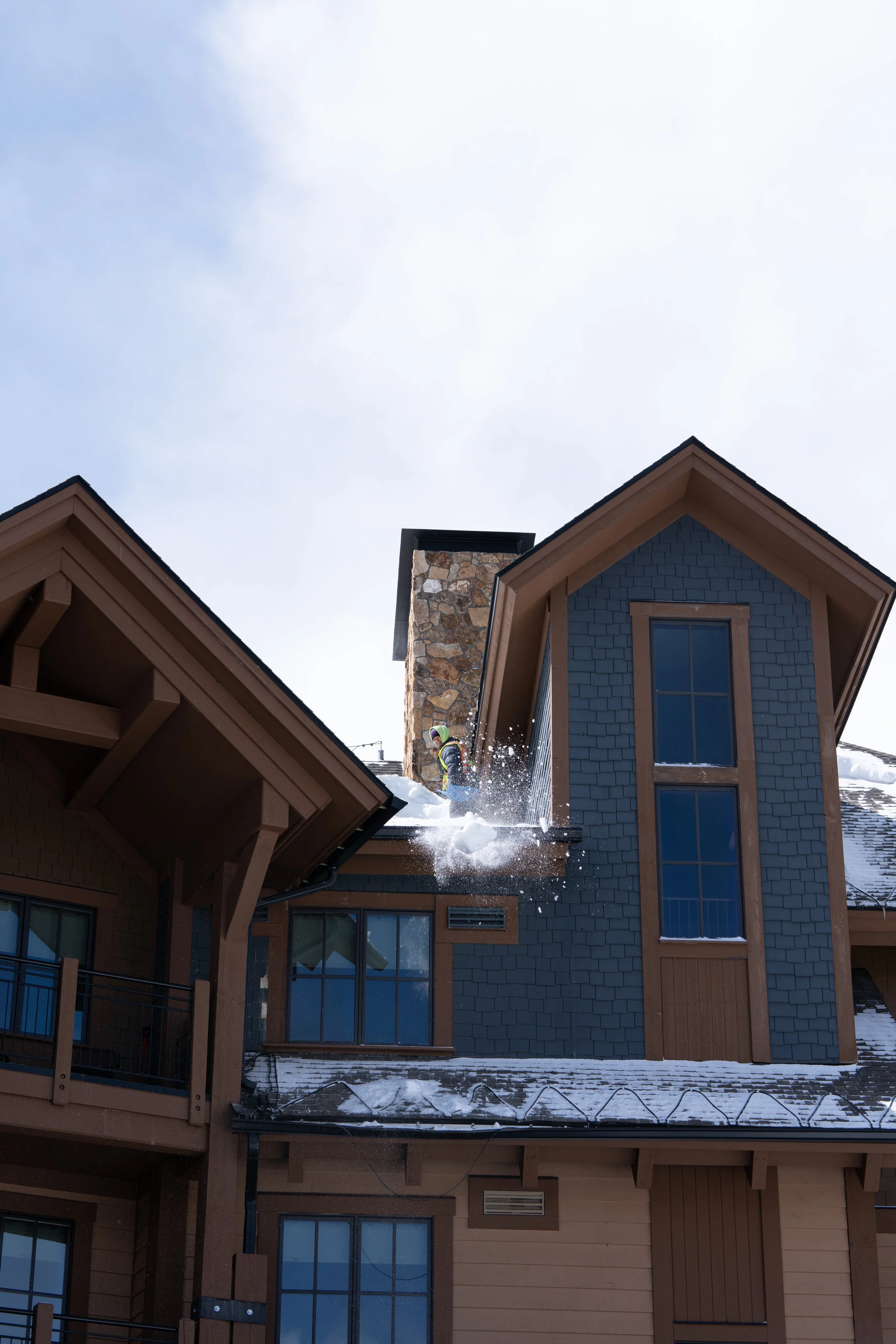 Turner Morris roofer shoveling snow off a roof of a multi-story house with stone chimney