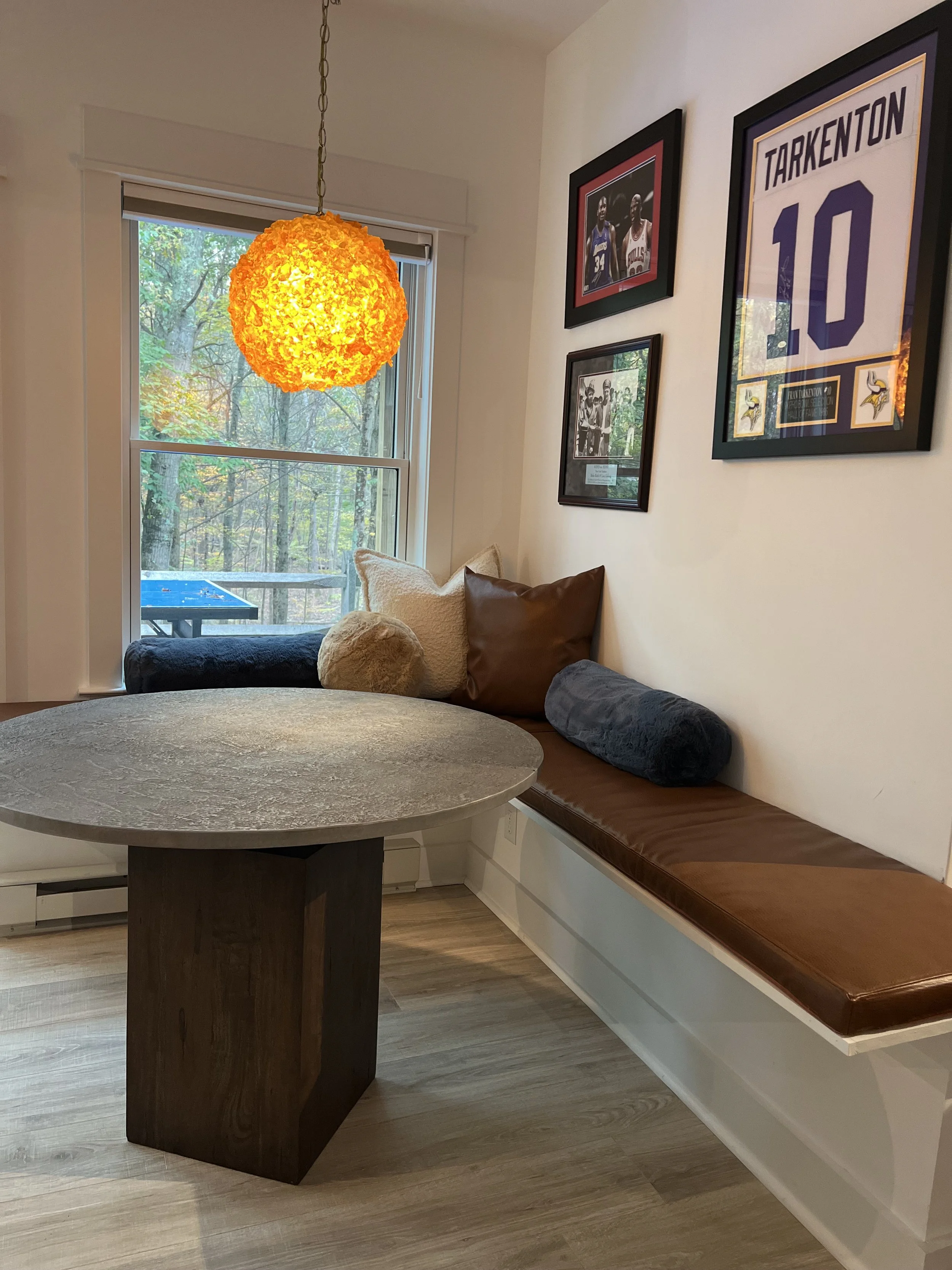 Corner with window seat cushions and framed sports memorabilia on the wall, illuminated by a hanging orange pendant light.