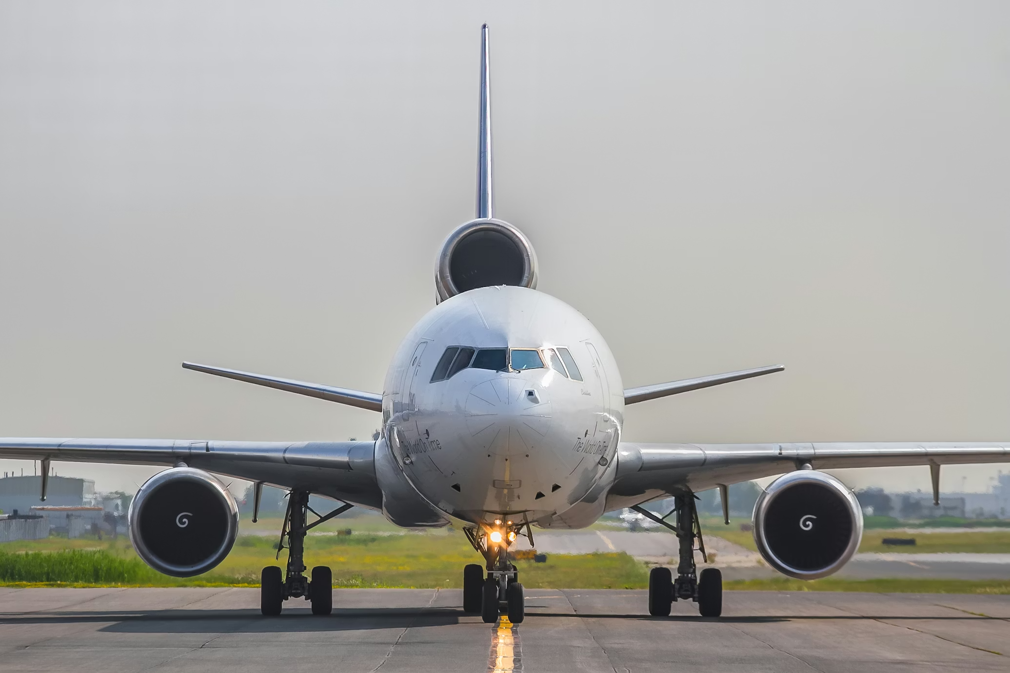 Front view of a white commercial airplane on the runway, with landing gear down and engines visible, under a cloudy sky.