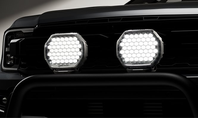Close-up of a vehicle's front, showing two large hexagonal LED headlights and a black grille.