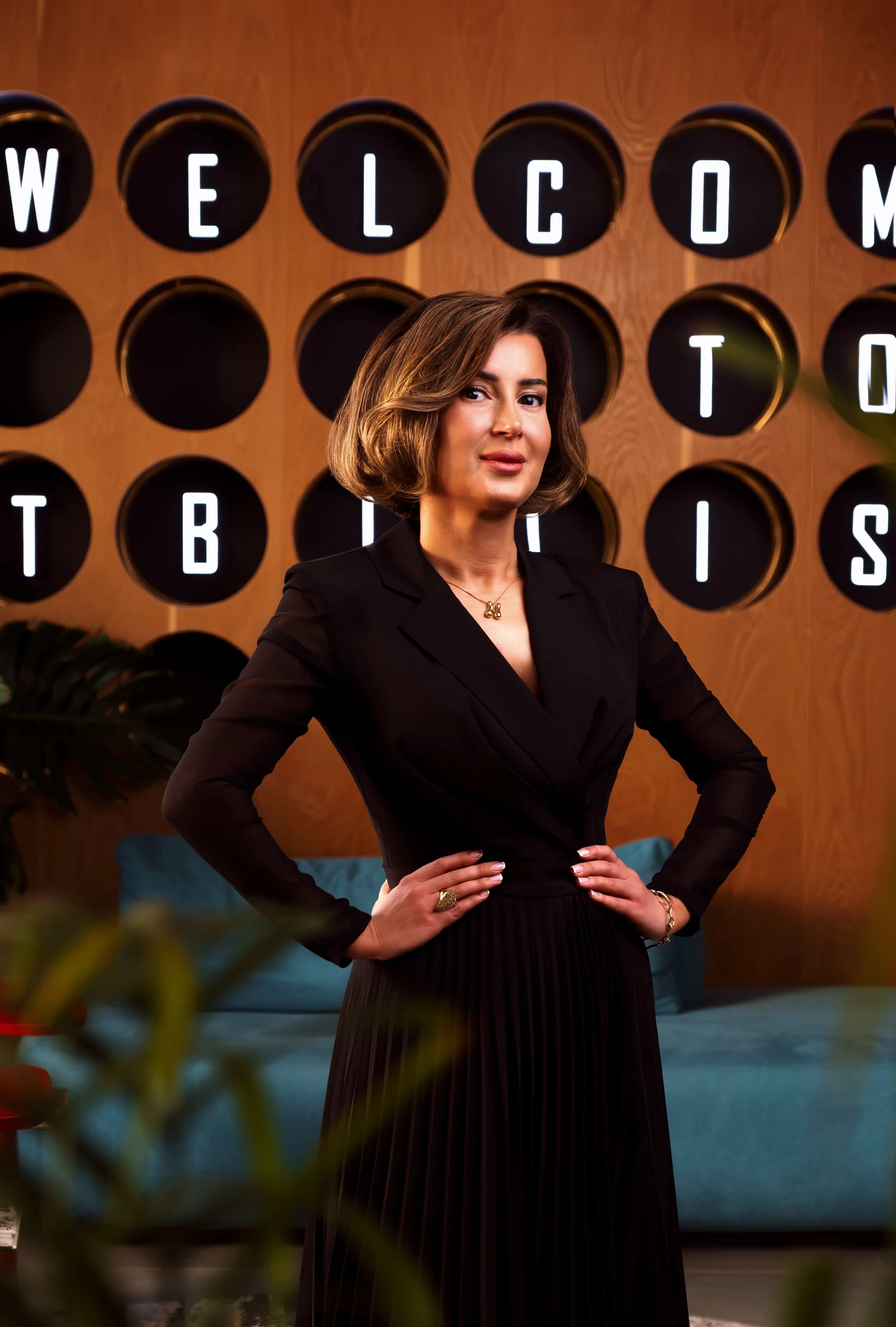 Portrait of Nina Gibbons in a black outfit, standing with hands on hips in front of circular wall lettering.