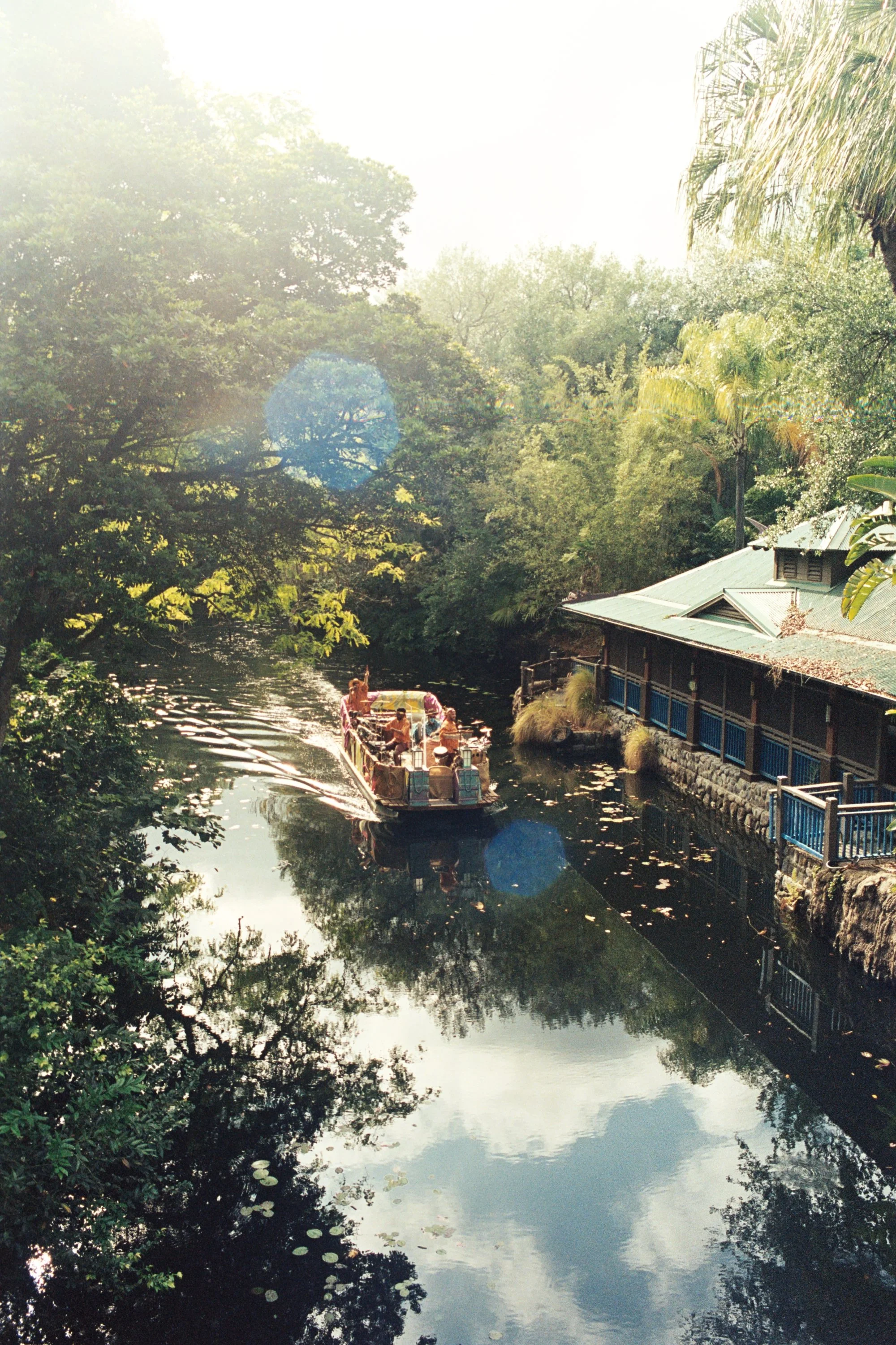 A boat with people on a river surrounded by lush green trees, with a building with a green roof on the right side.