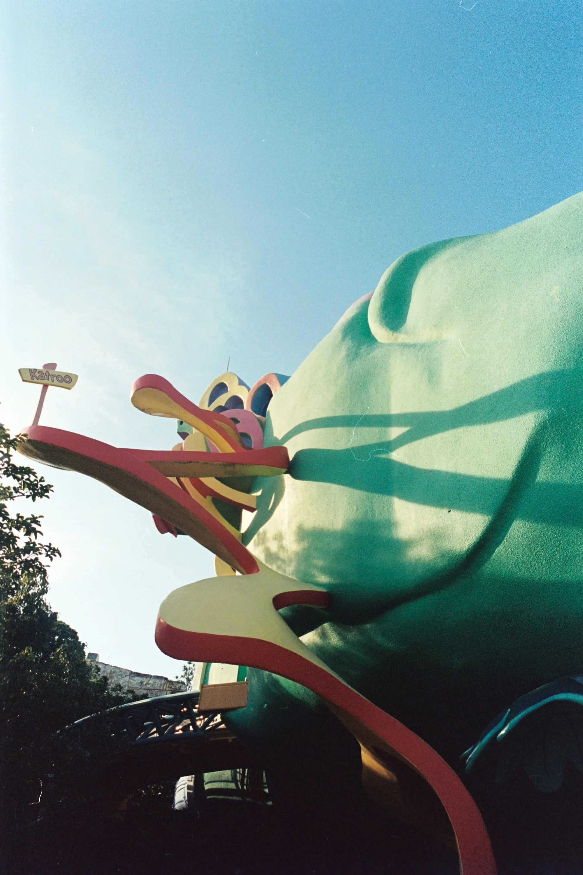 Colorful dragon slide at an amusement park with trees and a clear blue sky in the background.