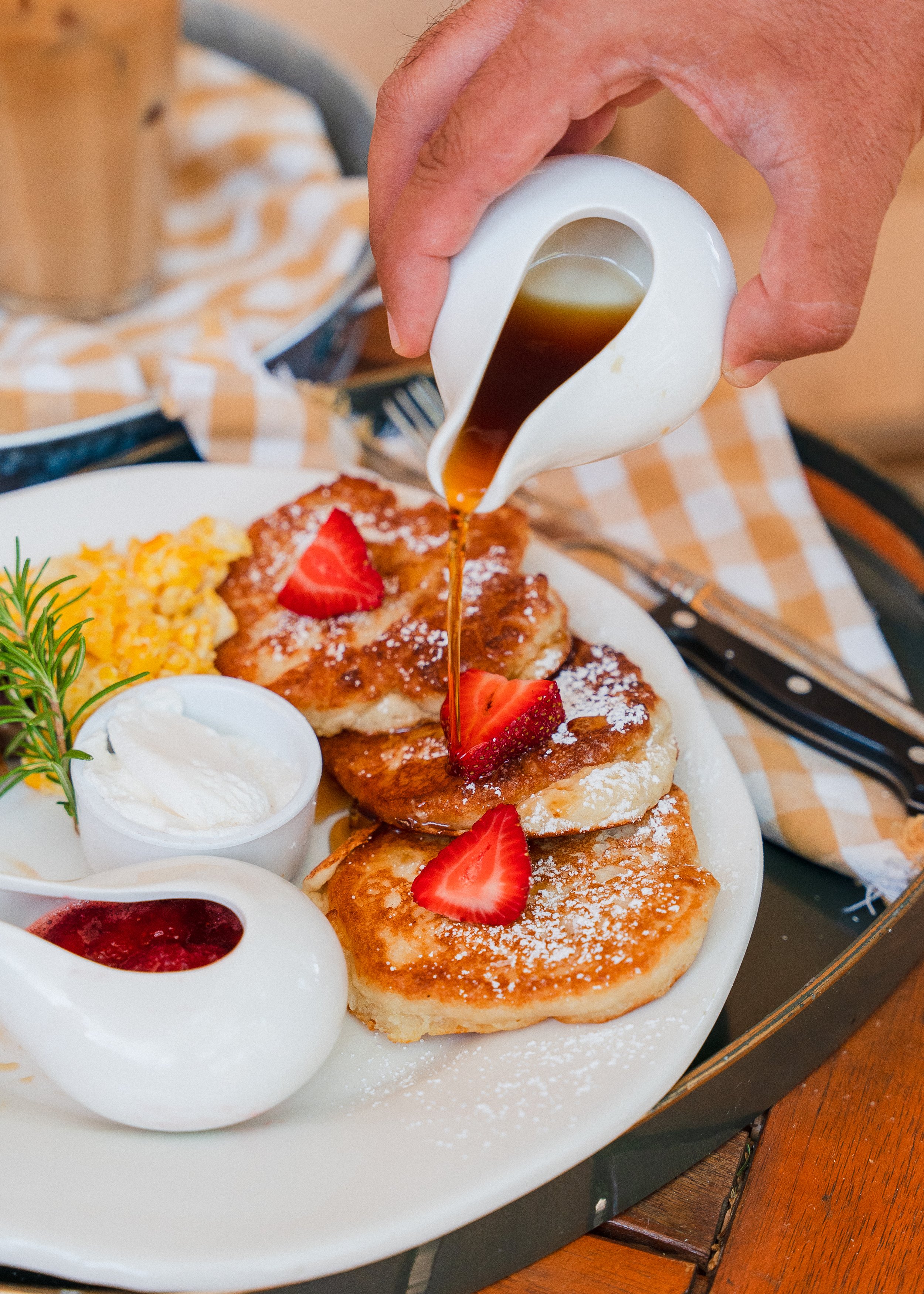 Hand pouring maple syrup over a stack of Chef Van's fluffy signature pancakes at The Good House in Desert Hot Springs.