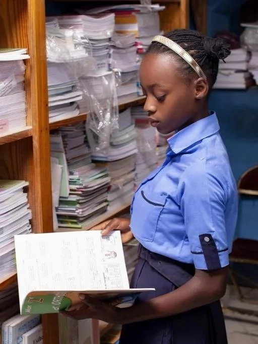 Haitian student in blue school uniform reading a book in a school library - EducNation Books To School program