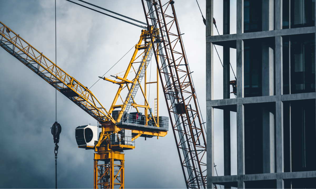 Yellow construction crane with the gray frame of a building under construction in the foreground.