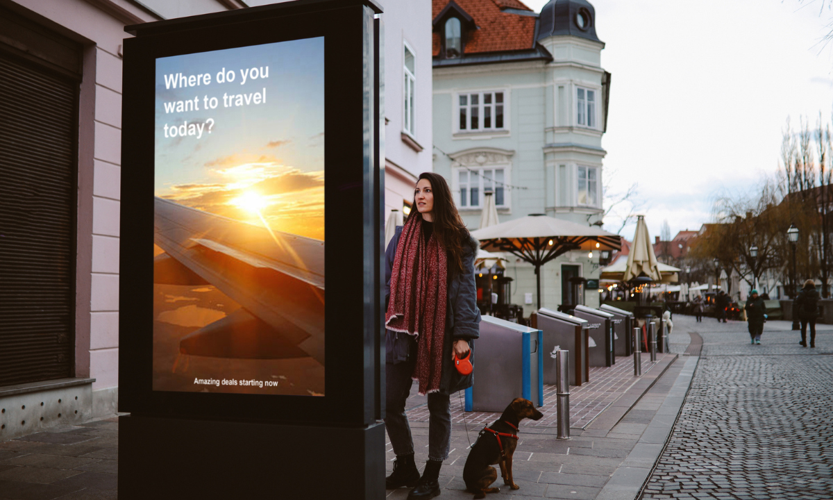 Young woman with her dog looking at a street-level OOH advertisement in a city centre.