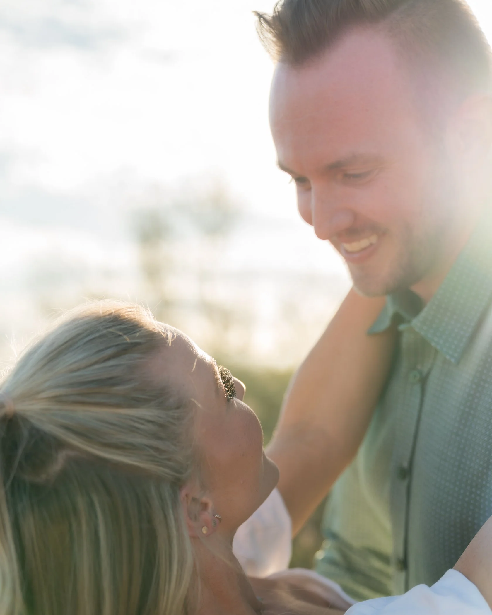 A man and woman smiling at each other outdoors during sunset.