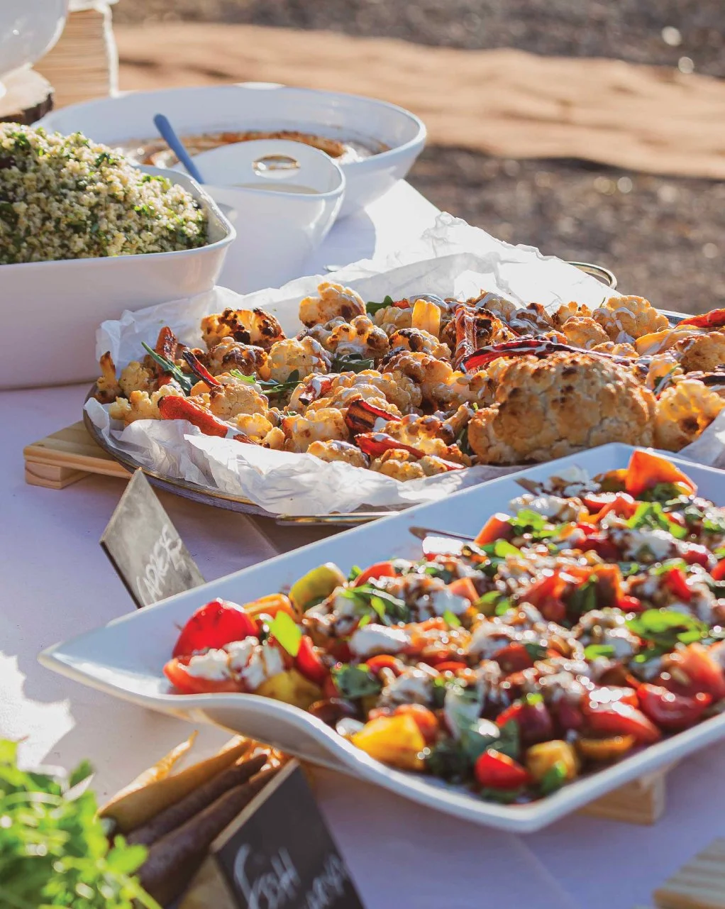 Outdoor summer buffet catering spread with roasted cauliflower, heirloom tomato salad, and herb quinoa