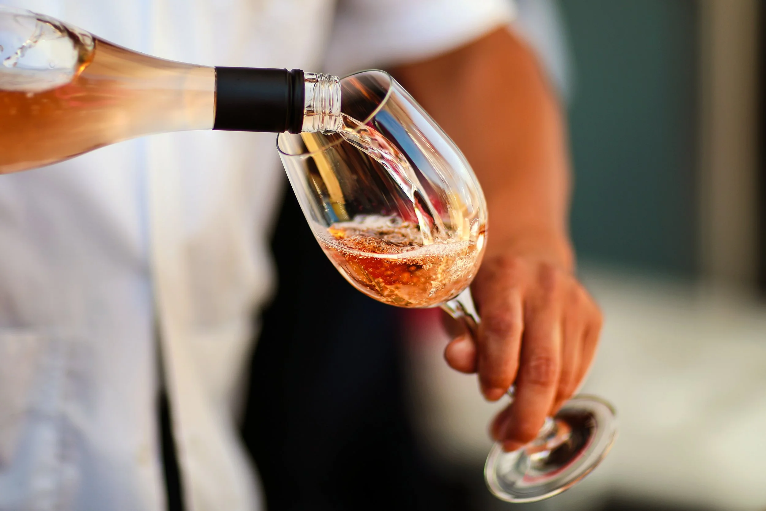 Person pouring rosé wine into a wine glass.