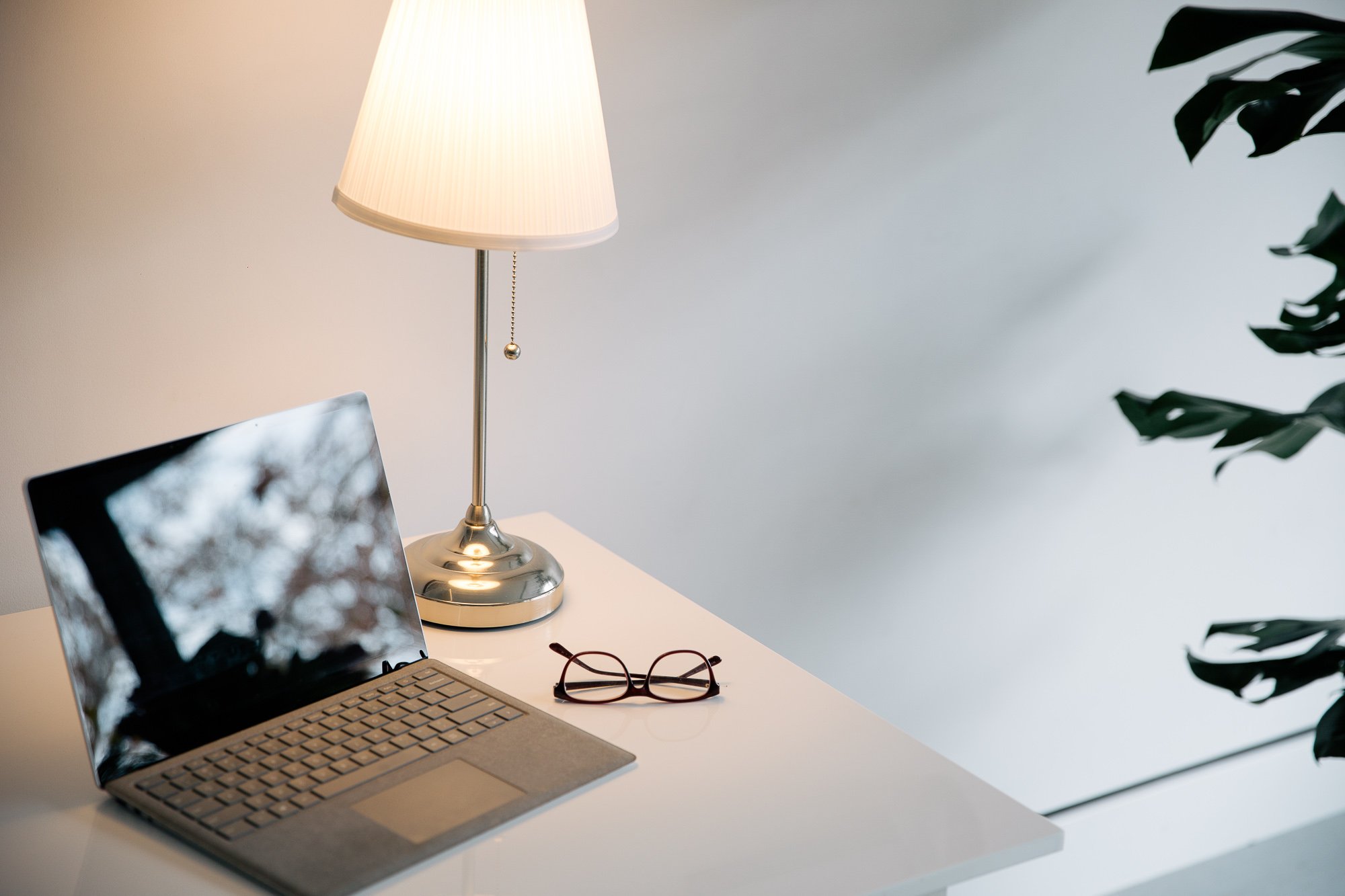 Desk with a laptop, a table lamp, and a pair of glasses in a minimalist setting.