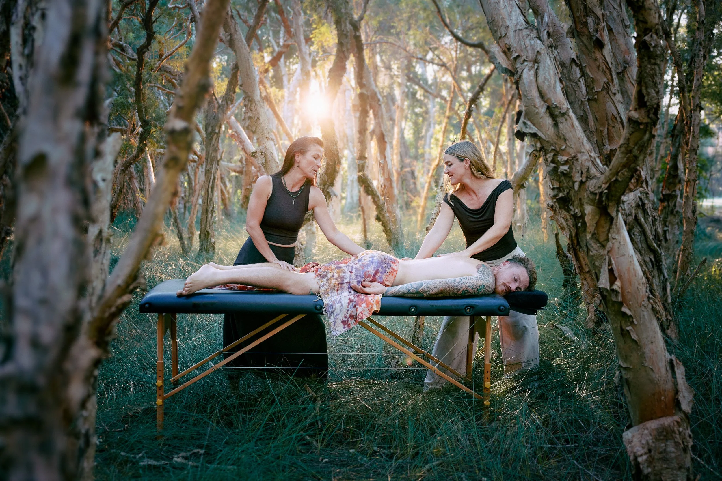Two masseuse giving a massage in a forest area with back sun