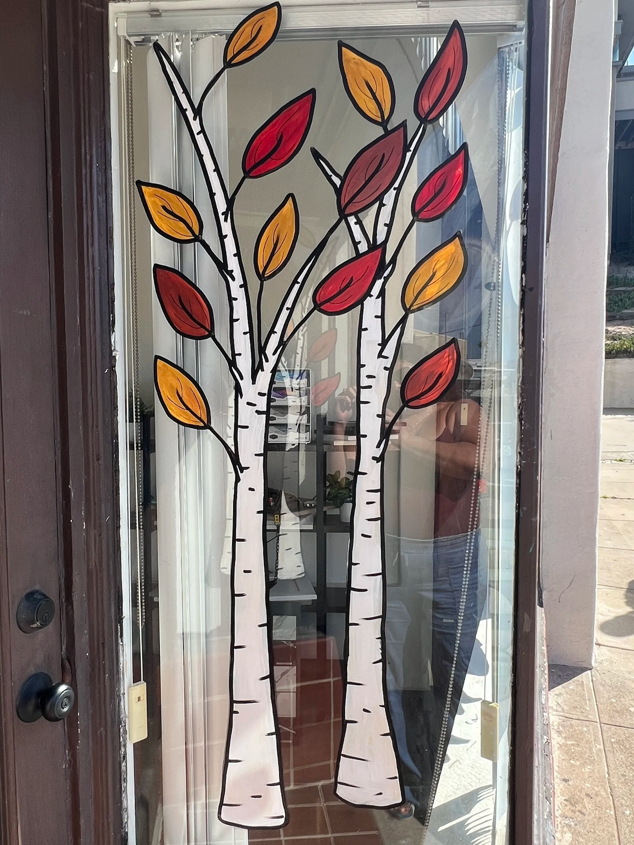 A large window decal depicting two stylized white birch trees with black outlines and orange, red, and yellow leaves.