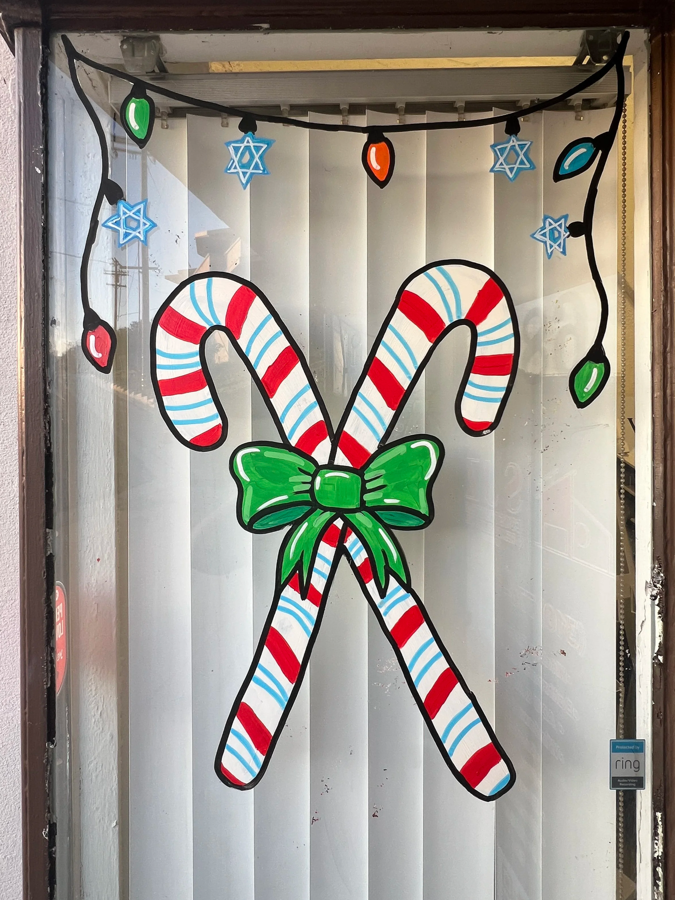 Decorative Christmas window display with large candy canes tied with a green bow, string lights, and snowflake ornaments.