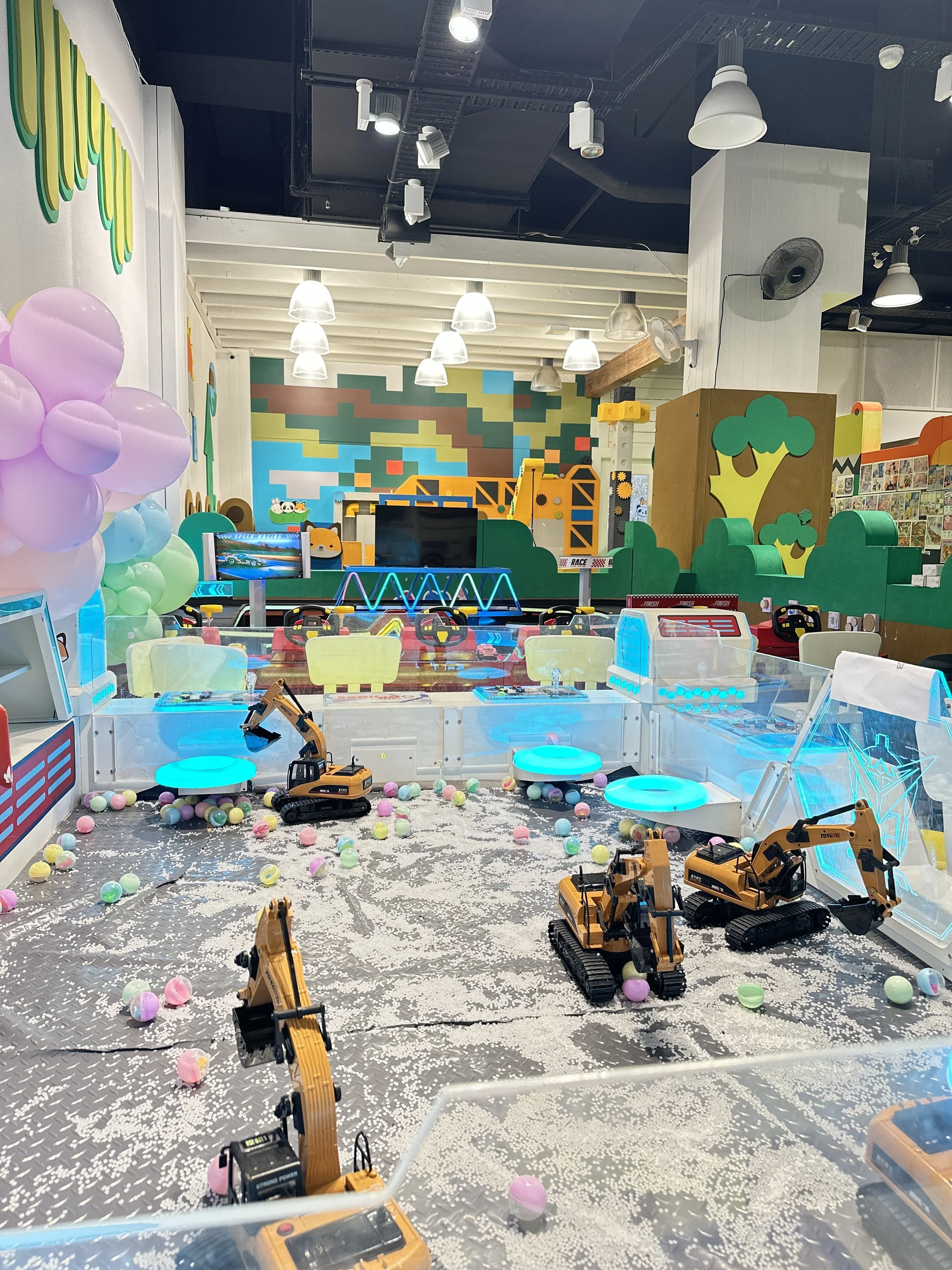 Indoor arcade with toy excavators, colorful balls, and bright lights in a playful setting.