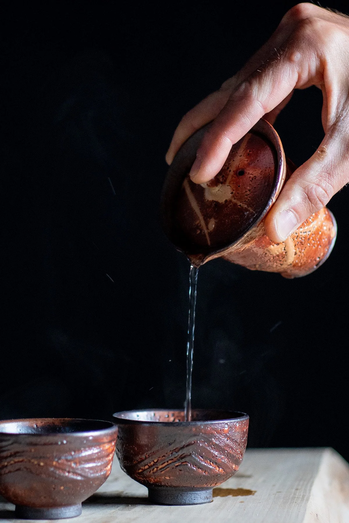 Pouring tea from a tall Shiboridashi teapot into handmade ceramic cups during a quiet daily tea ritual.