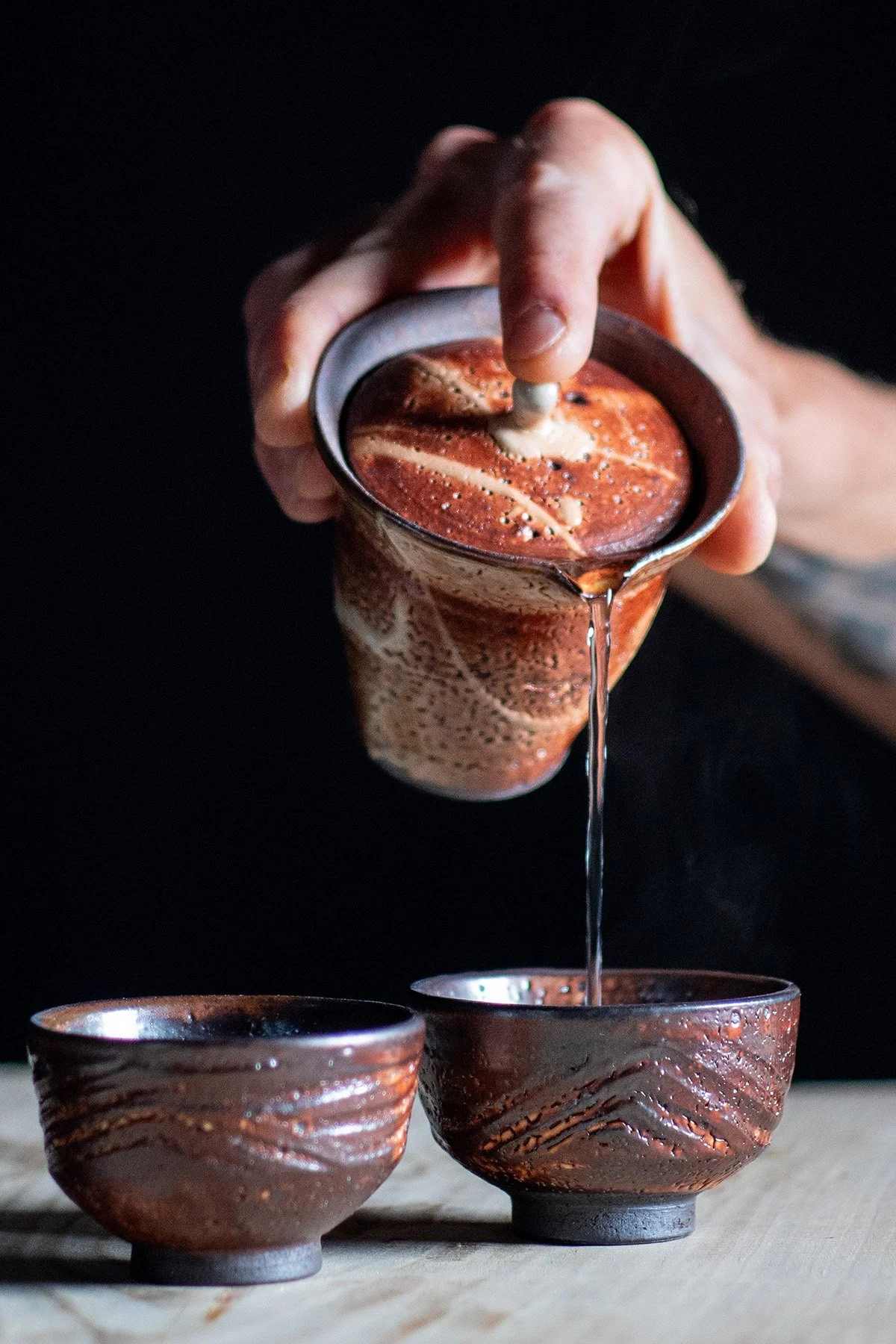 Pouring tea from a tall Shiboridashi teapot into handmade ceramic cups during a quiet daily tea ritual.