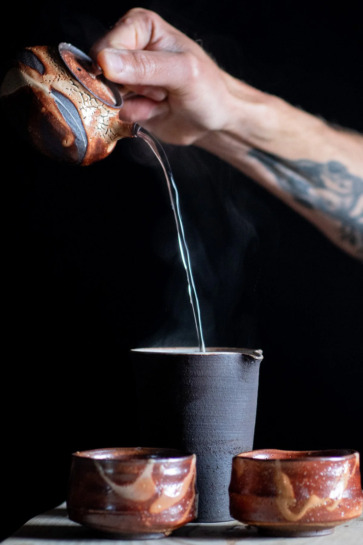 Pouring tea from a Kyusu teapot into handmade ceramic cups during a quiet daily tea ritual.