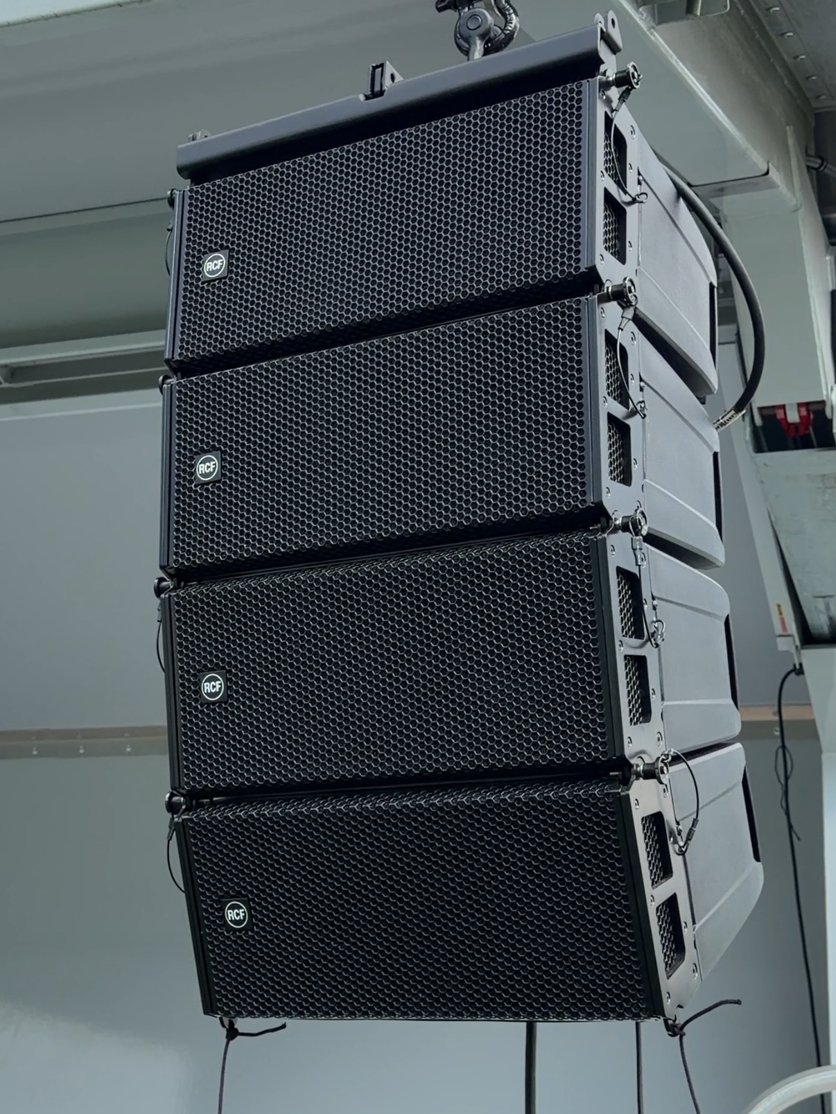 A vertical stack of four black professional line array speakers, hanging.