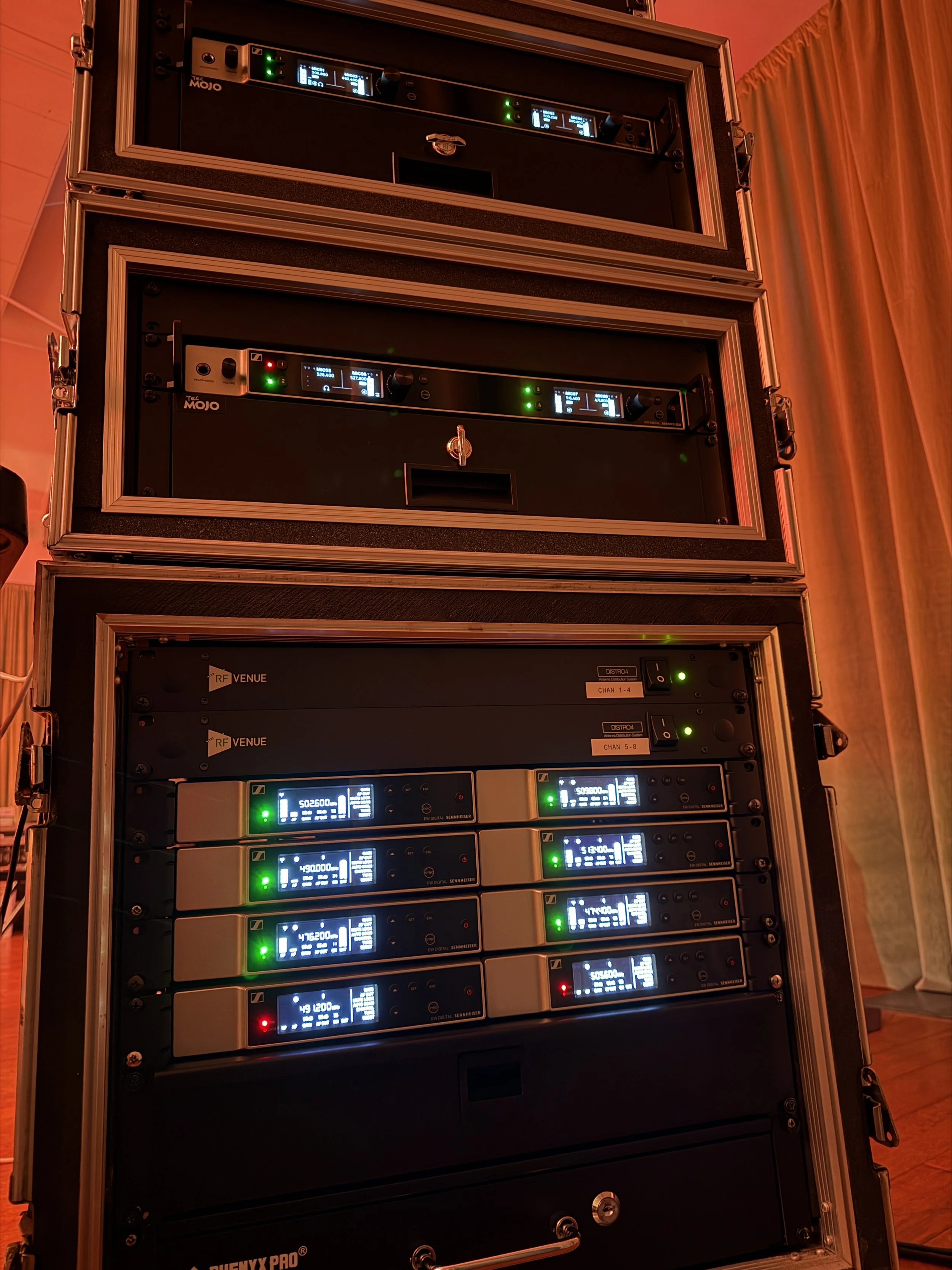 Audio equipment in a rack, including several digital wireless microphone receivers with illuminated displays and status lights, in a professional audio setup.