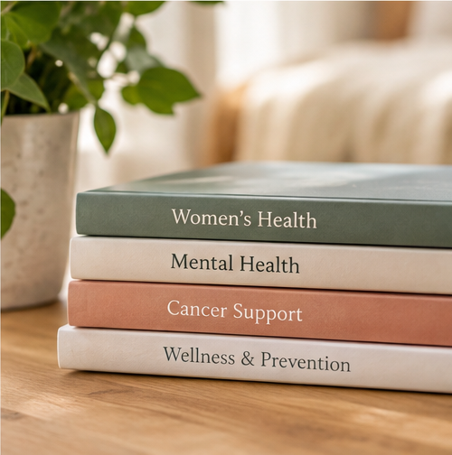 A stack of books titled "Women's Health", "Mental Health", "Cancer Support", and "Wellness & Prevention" sit on an oak table.