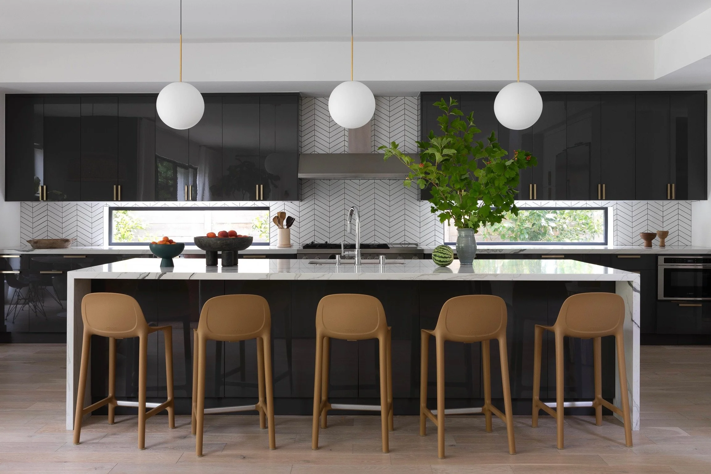 Los Angeles modern kitchen with black cabinetry, marble waterfall island, globe pendant lighting and warm wood counter stools.